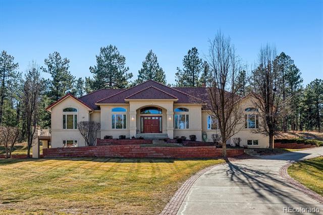 Large beige house with a red tile roof, arched entrance, brick retaining wall, and curved driveway.