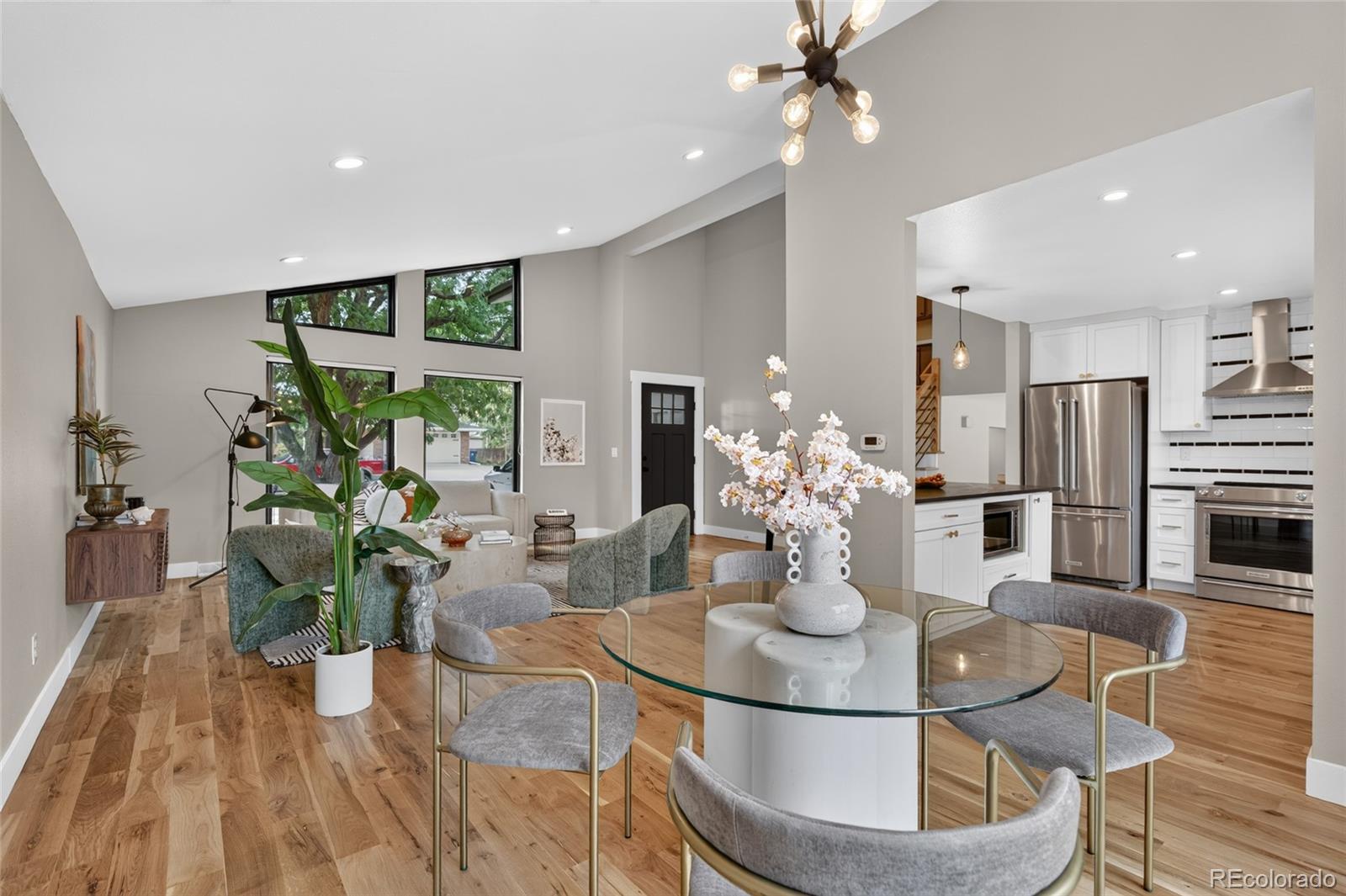 Open-plan living and dining area with tall windows, hardwood floors, and a modern white kitchen.