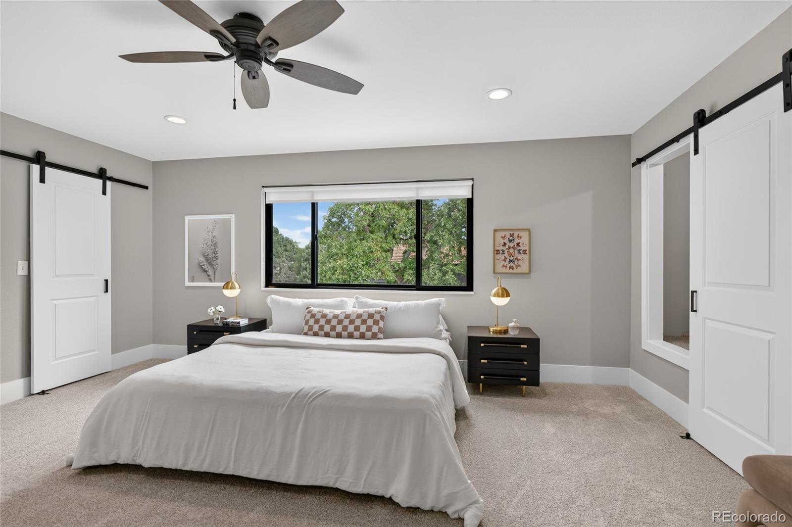 Staged bedroom with a white bed beneath a wide window and white sliding barn doors.