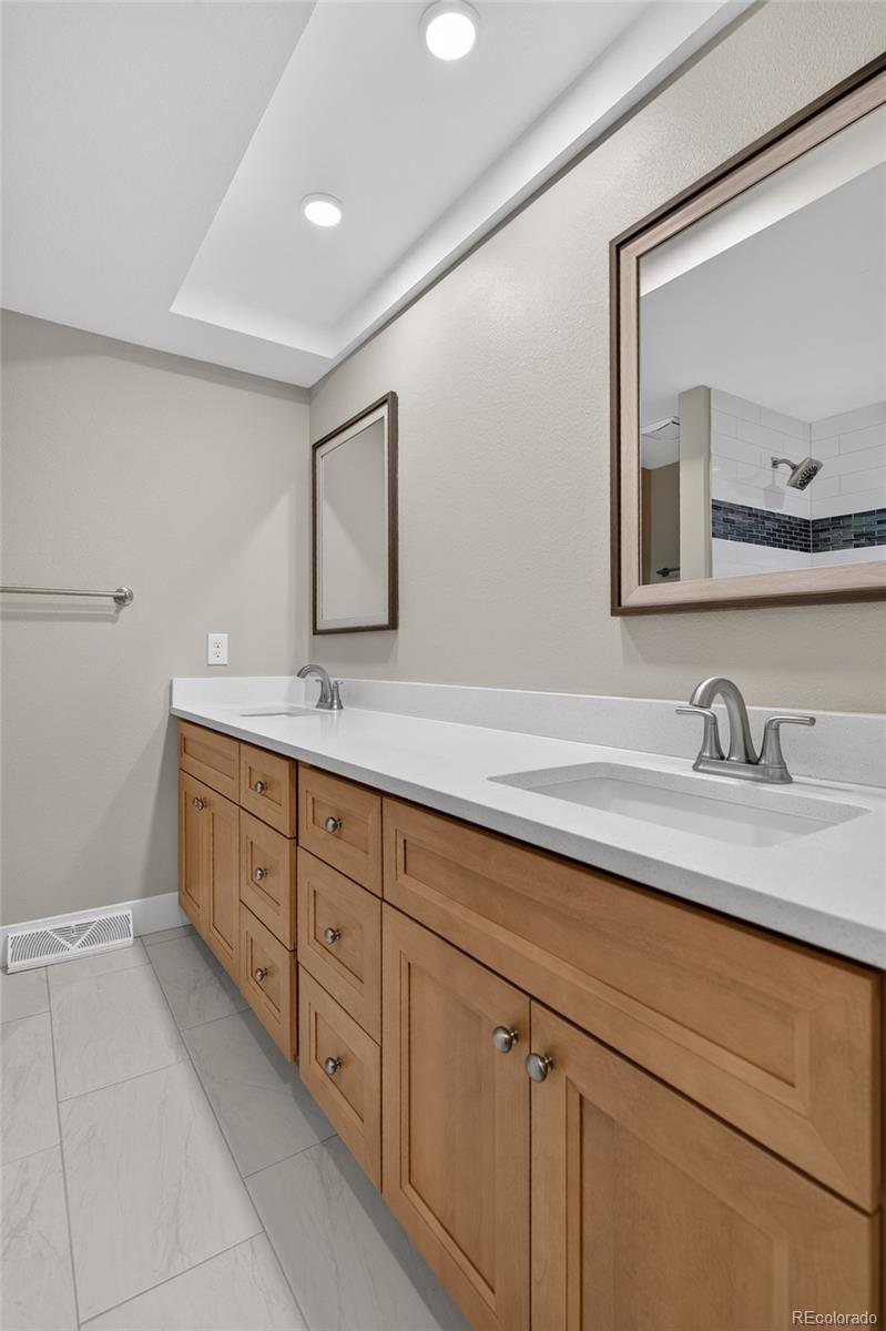 Bathroom with a long double-sink vanity, light wood cabinets, and mirrors reflecting a tiled shower.