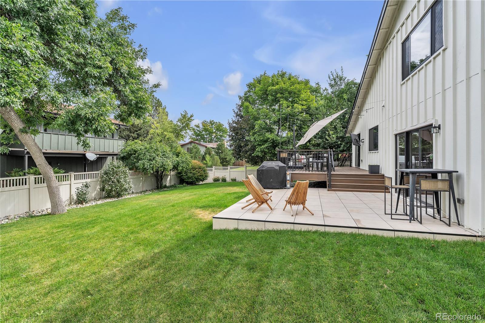 Backyard with a tiled patio, raised deck, outdoor furniture, and a broad green lawn.