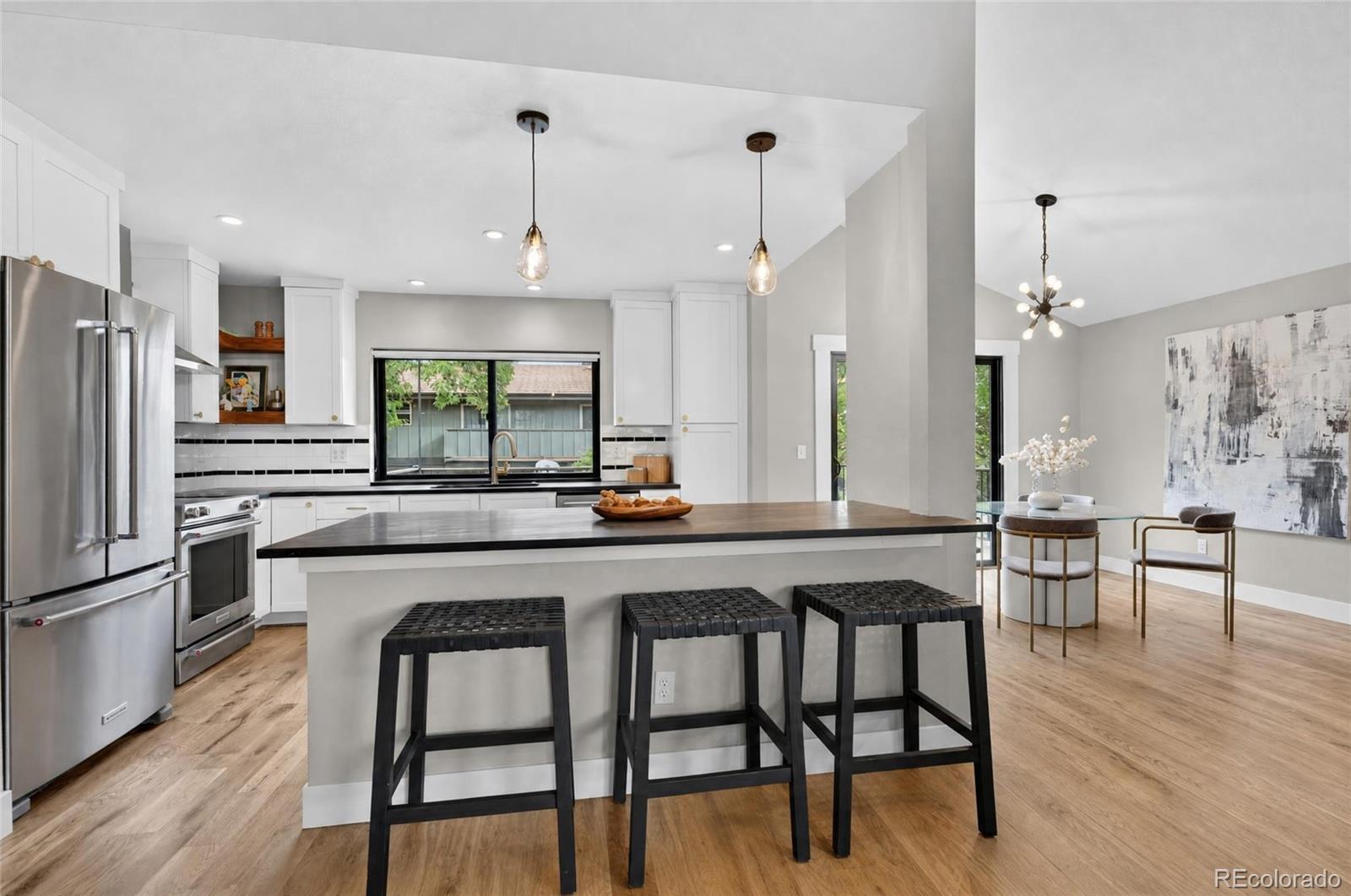 Open kitchen with white cabinets, stainless steel appliances, and a large island with three stools.