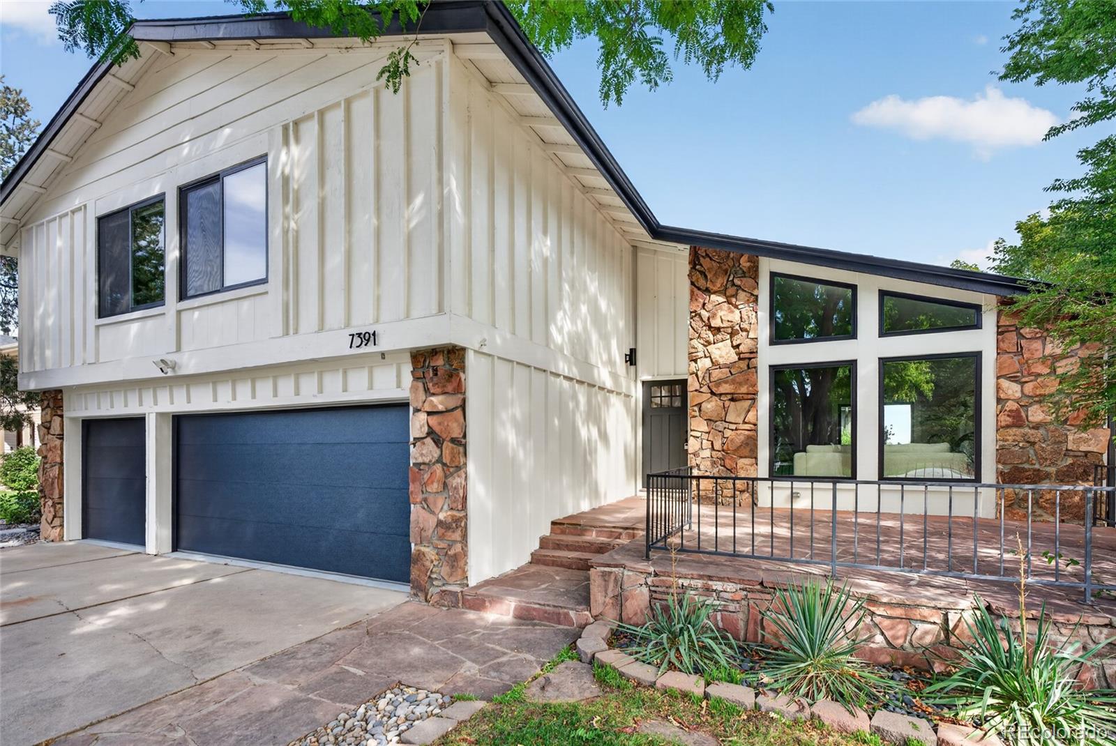 White-sided home with stone accents, blue double garage door, and raised patio.