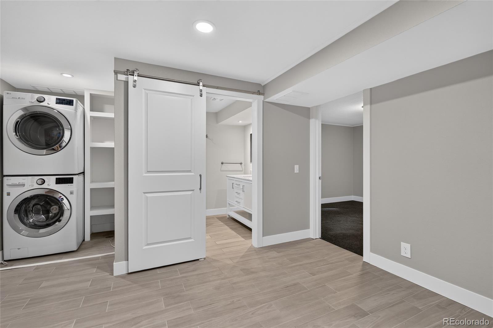 Laundry area with stacked washer and dryer, open shelving, and sliding barn-style door.