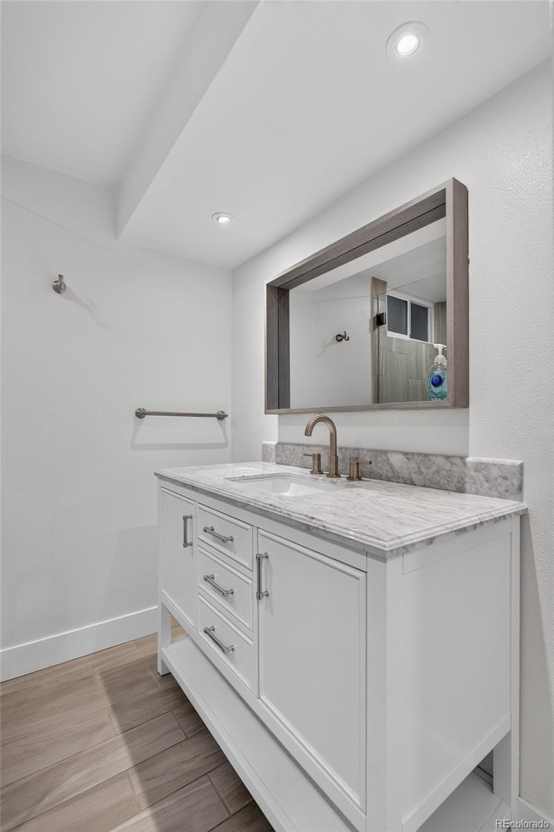 Bathroom vanity with a gray-veined stone countertop, bronze faucet, and large wood-framed mirror.