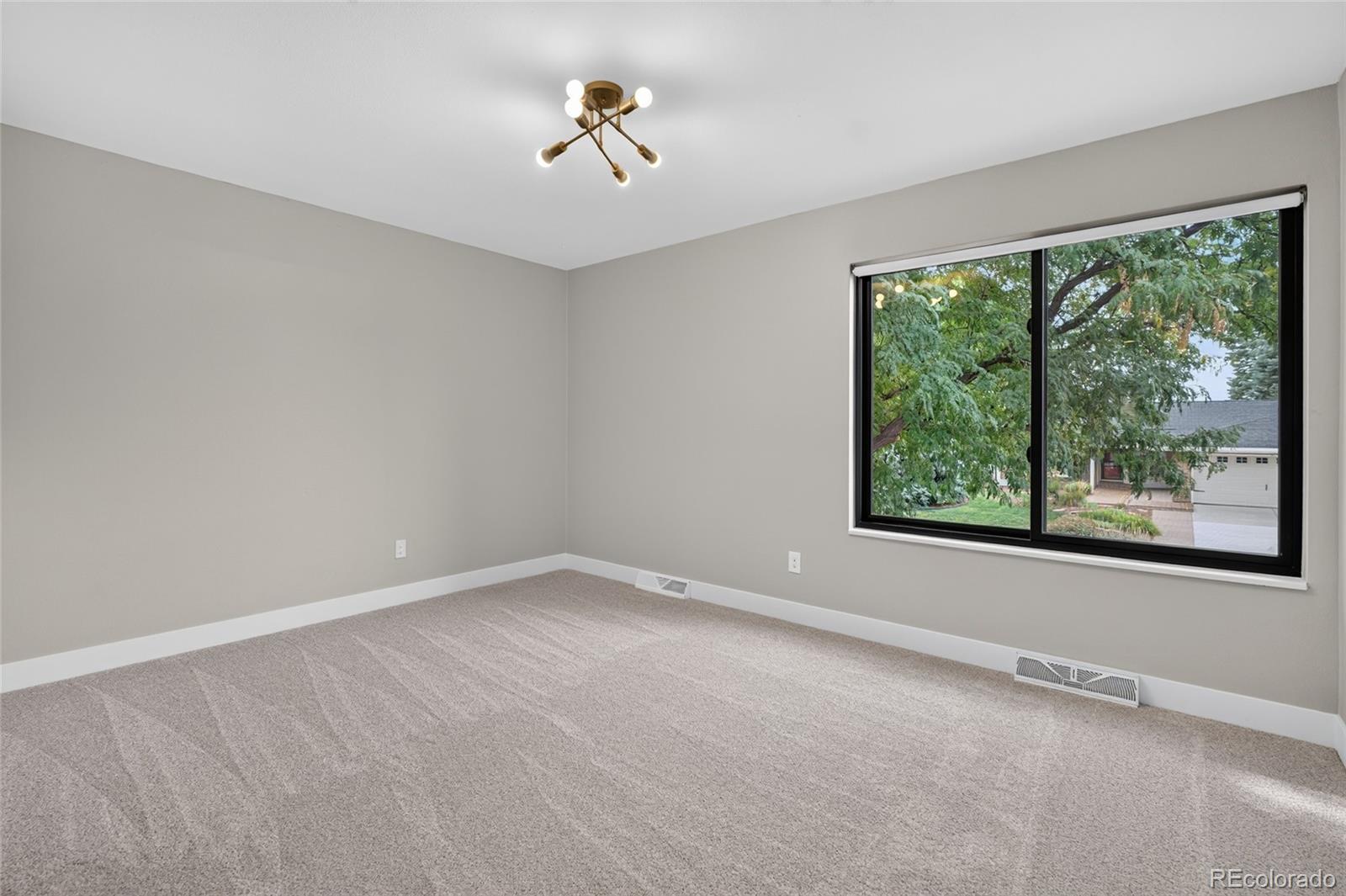 Empty carpeted bedroom with a large window overlooking leafy trees.