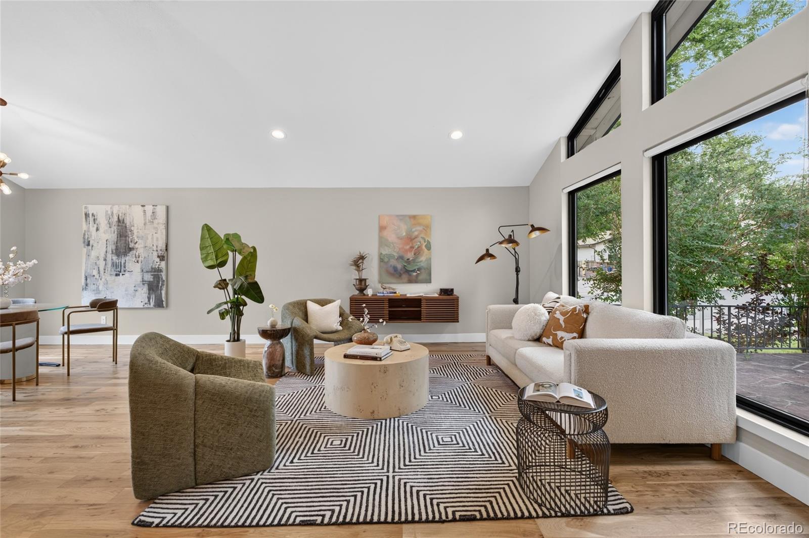 Staged living room with tall windows, neutral seating, light wood floors, and a geometric rug.