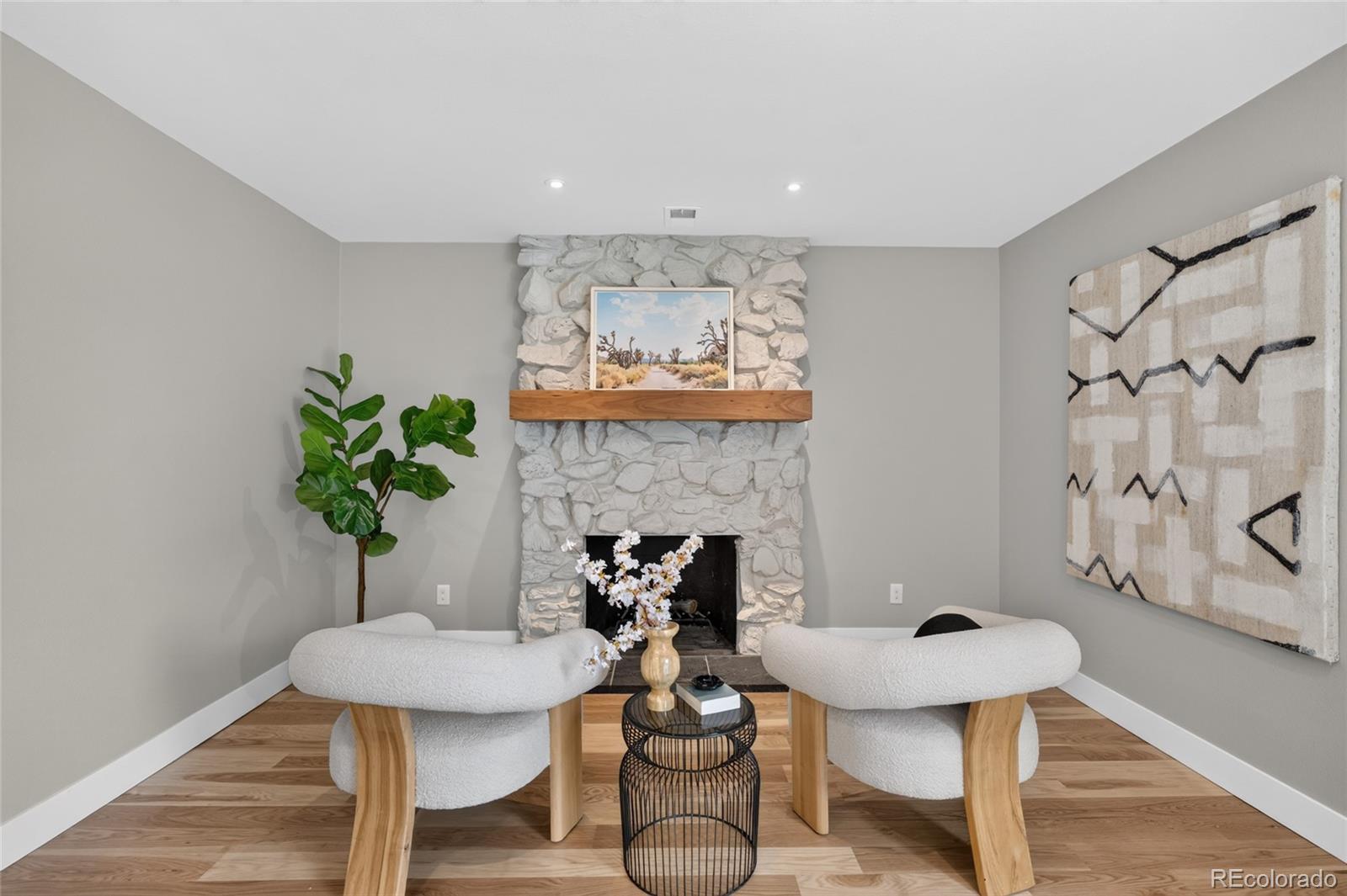 Staged living room with a white stone fireplace, wood mantel, and two curved chairs.