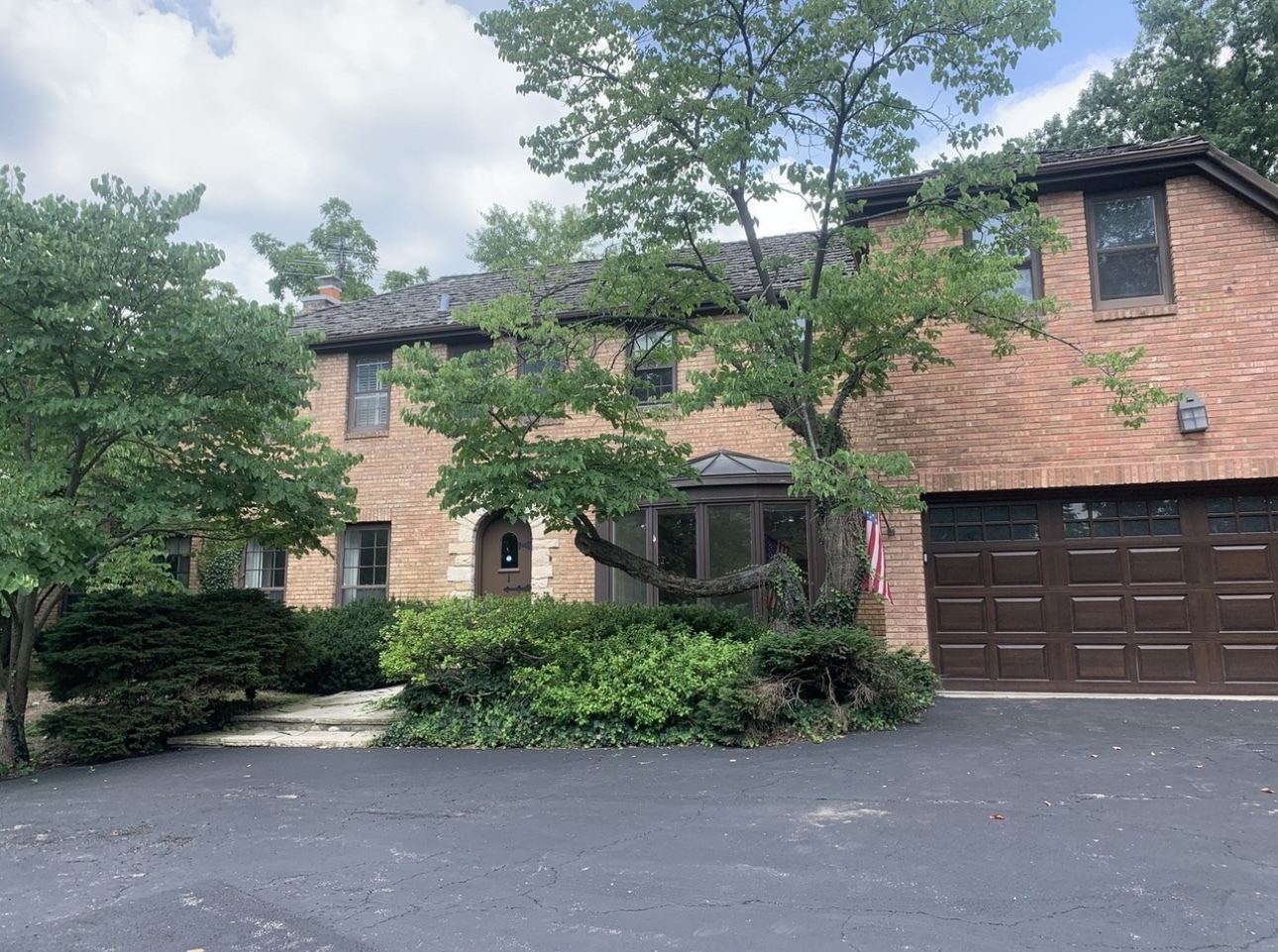 Two-story brick house with a double garage, mature trees, and landscaped front entry.