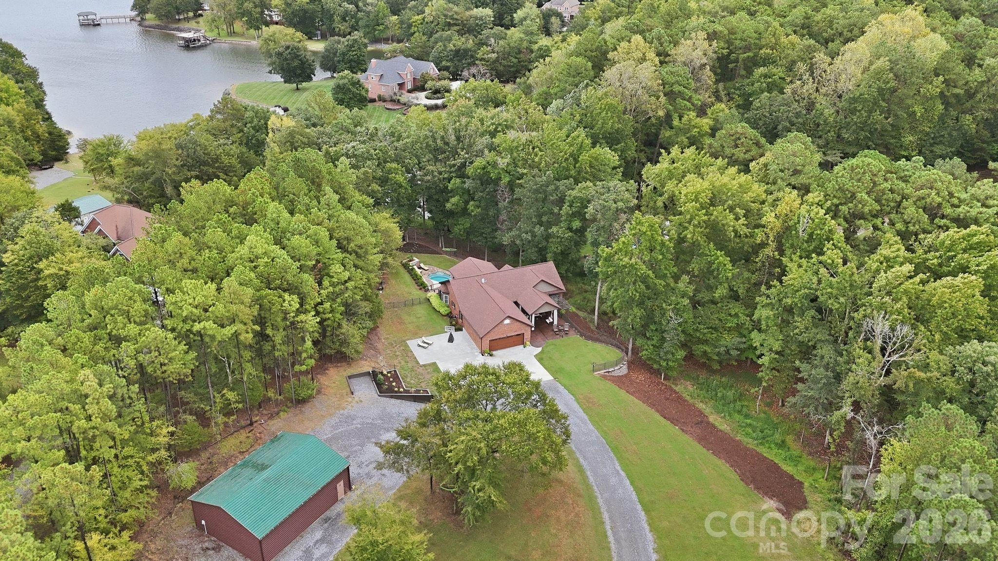 Aerial view of a brick home and pool surrounded by trees near a lake.