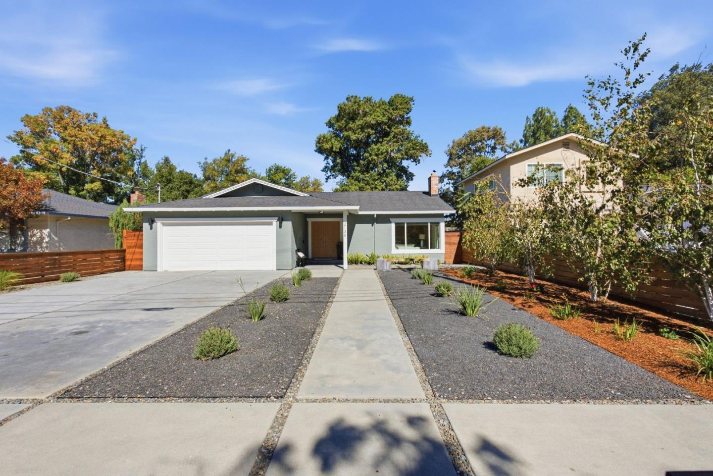 Single-story gray house with a white garage door, landscaped front yard, and wood fencing.