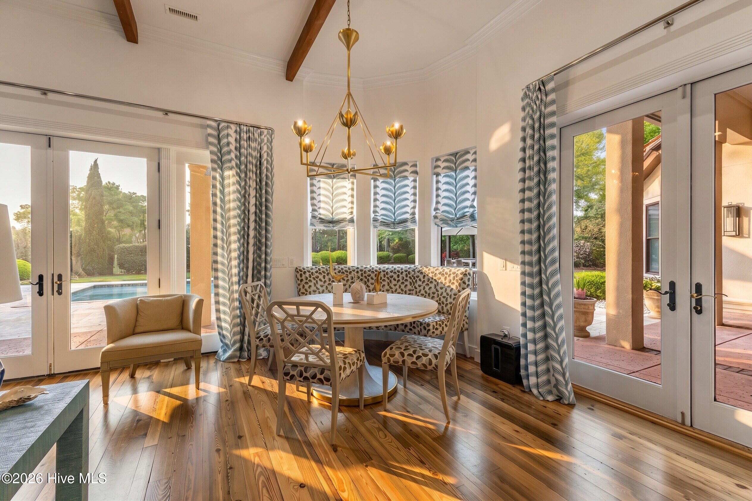 Dining room with a round table, patterned banquette, brass chandelier, and glass doors opening to a pool patio.