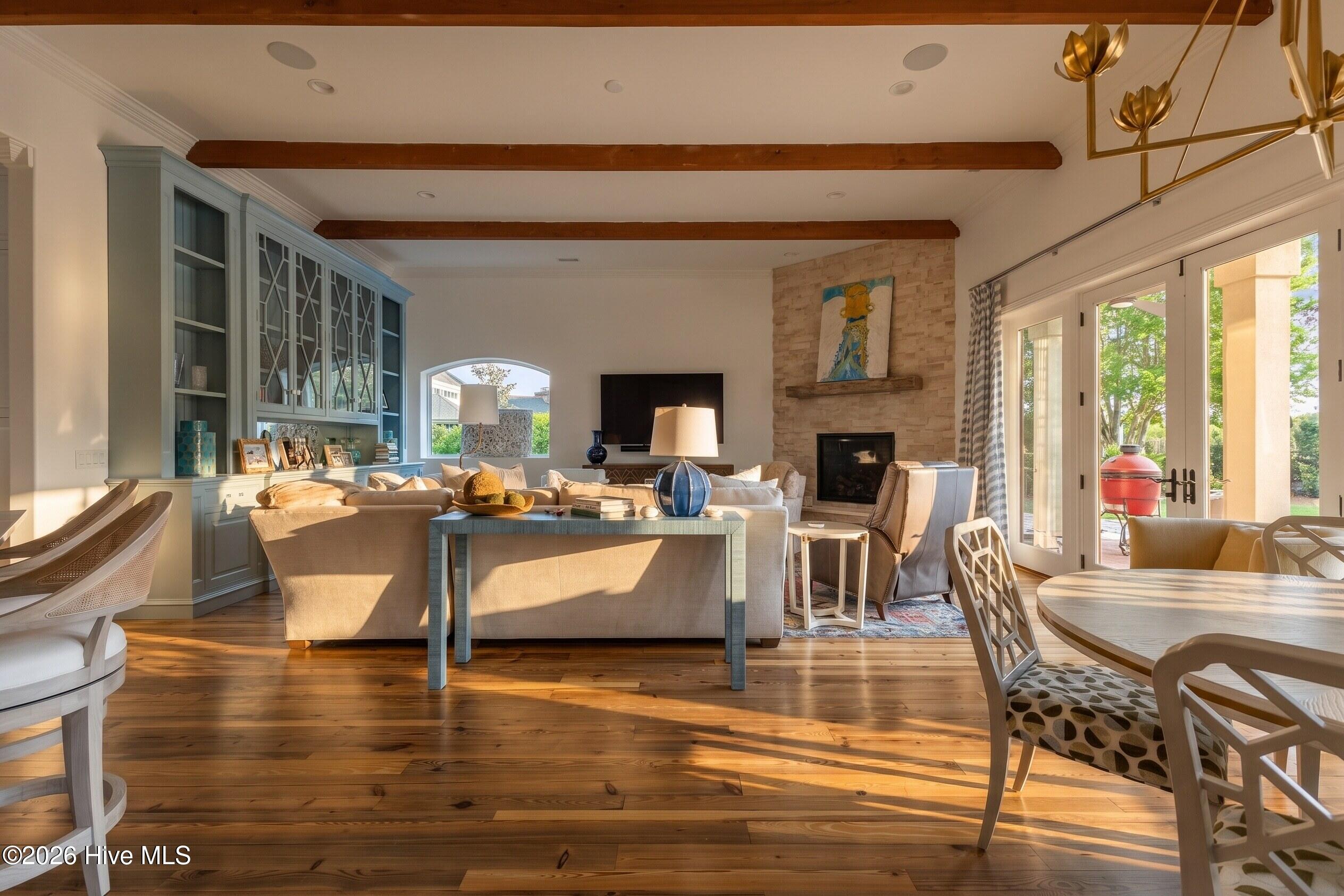 Living room with exposed wood beams, blue built-ins, a stone fireplace, and doors to the patio.