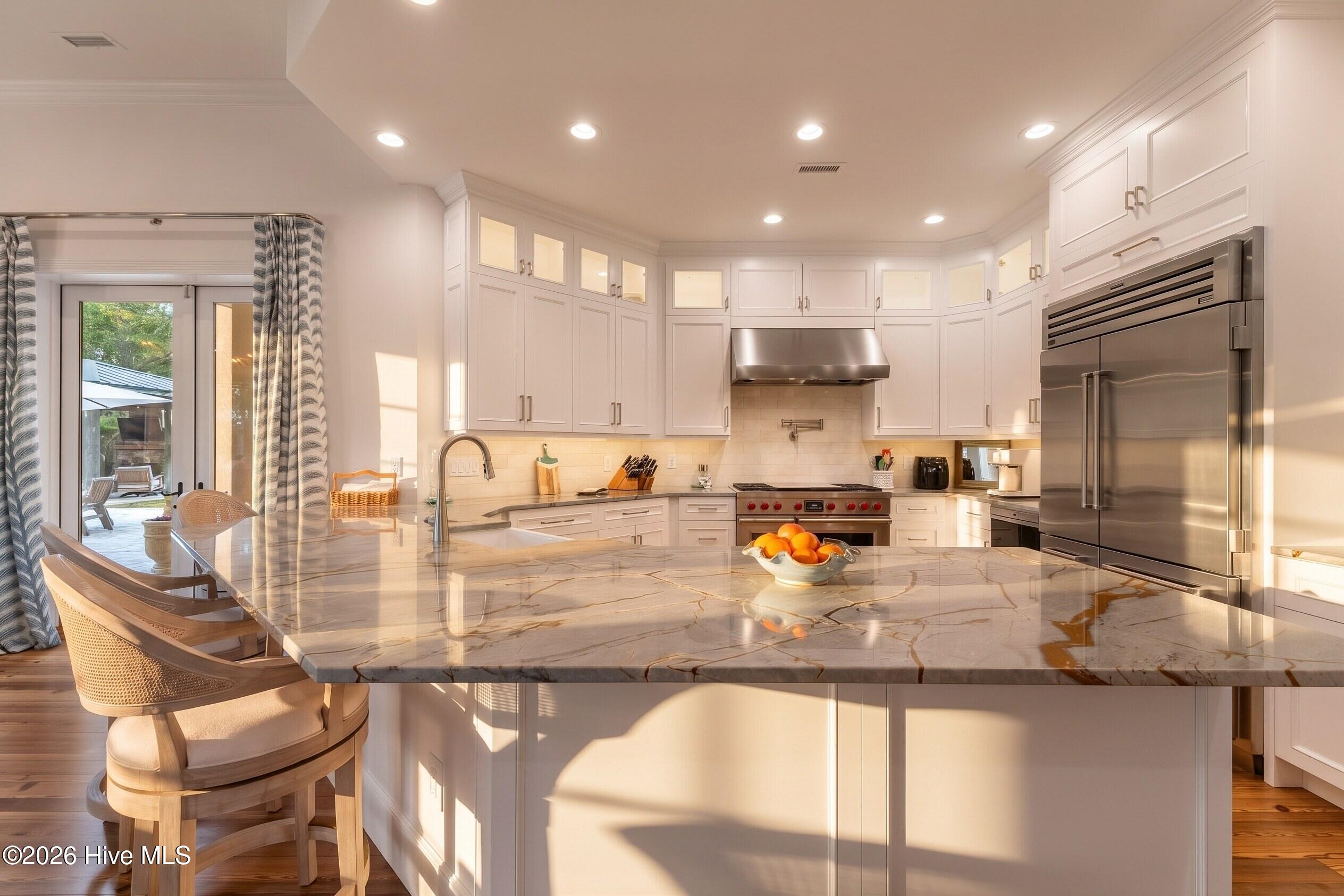 Bright white kitchen with a large veined stone island and stainless steel appliances.