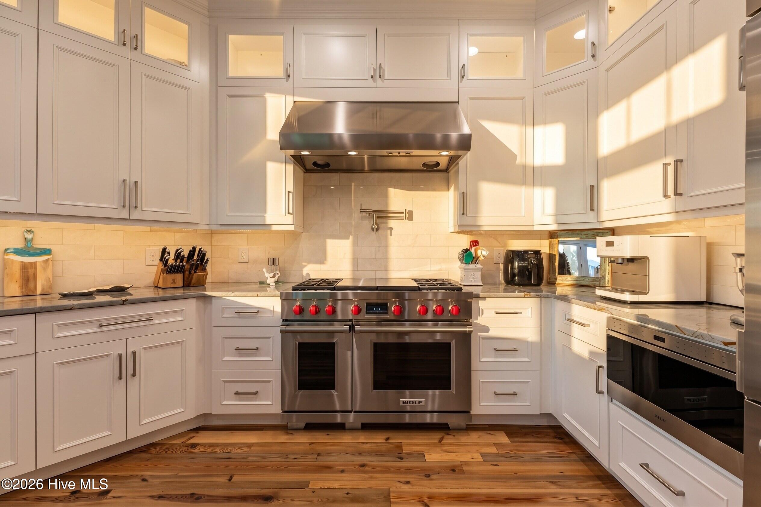 Kitchen with white cabinetry, a stainless steel Wolf range, and warm wood plank flooring.