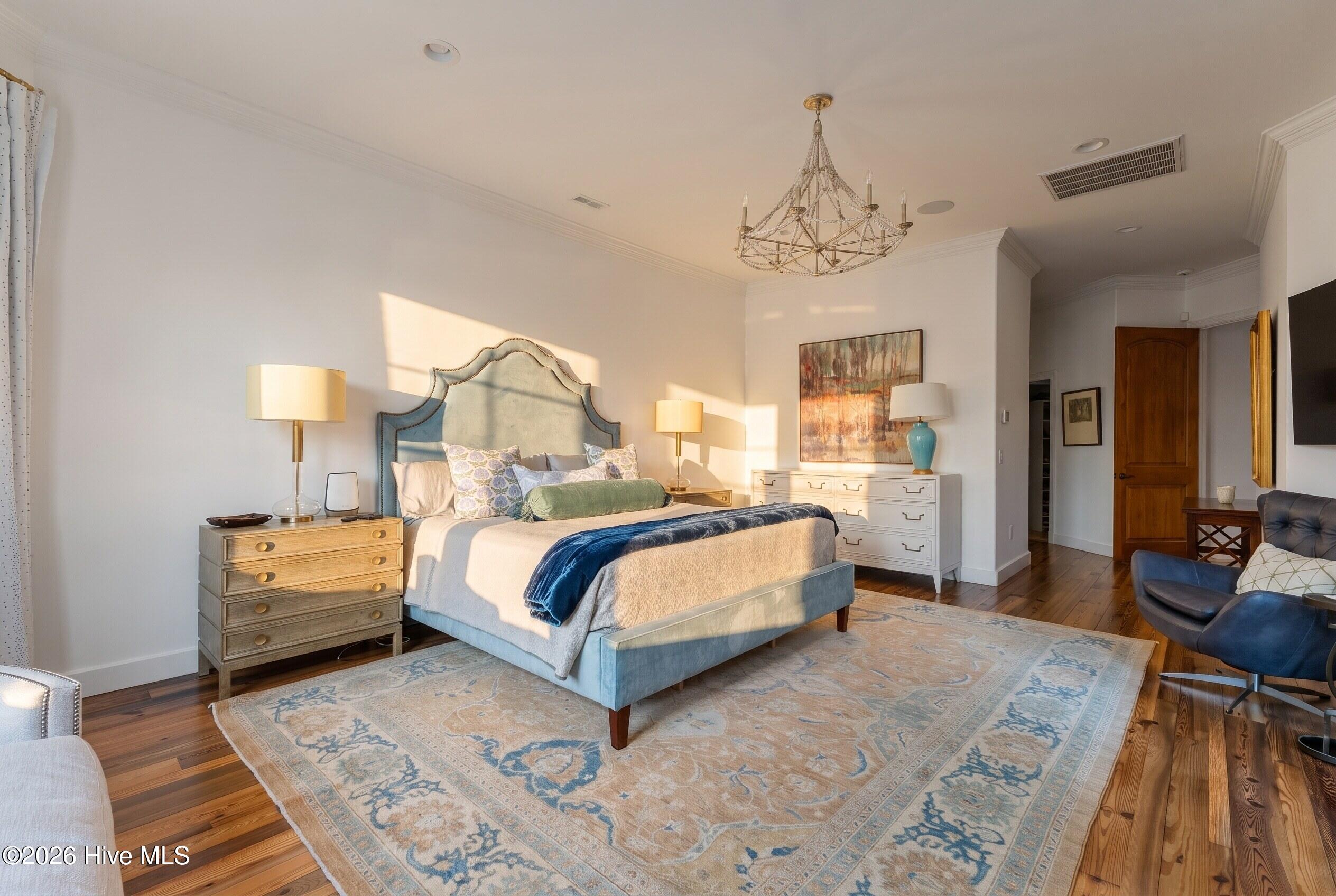 Furnished bedroom with a blue upholstered bed, patterned rug, wood floors, and sunlight across the bed.