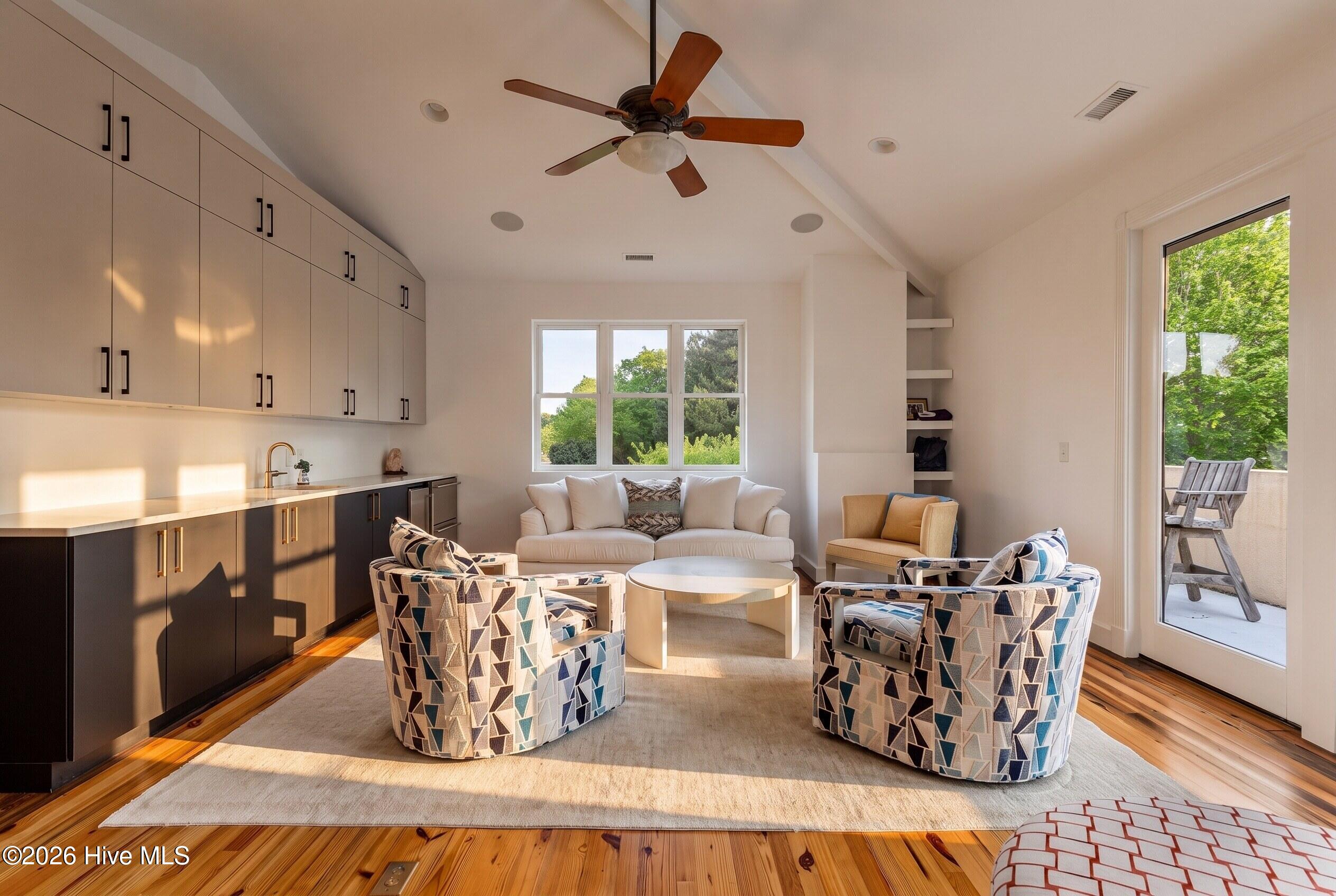 Living room with a kitchenette, geometric armchairs, a white sofa, and a glass door to the patio.