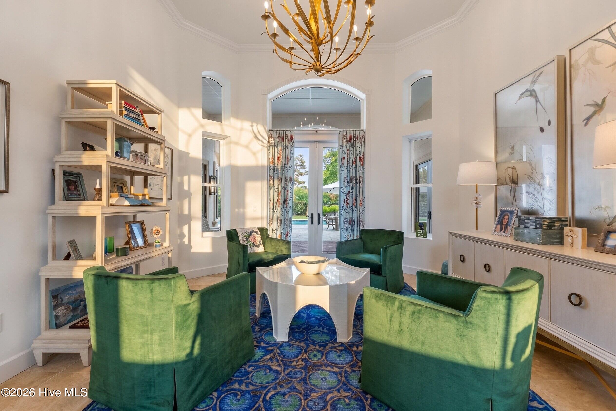 Sitting room with green velvet chairs, a blue patterned rug, and French doors opening to a patio.
