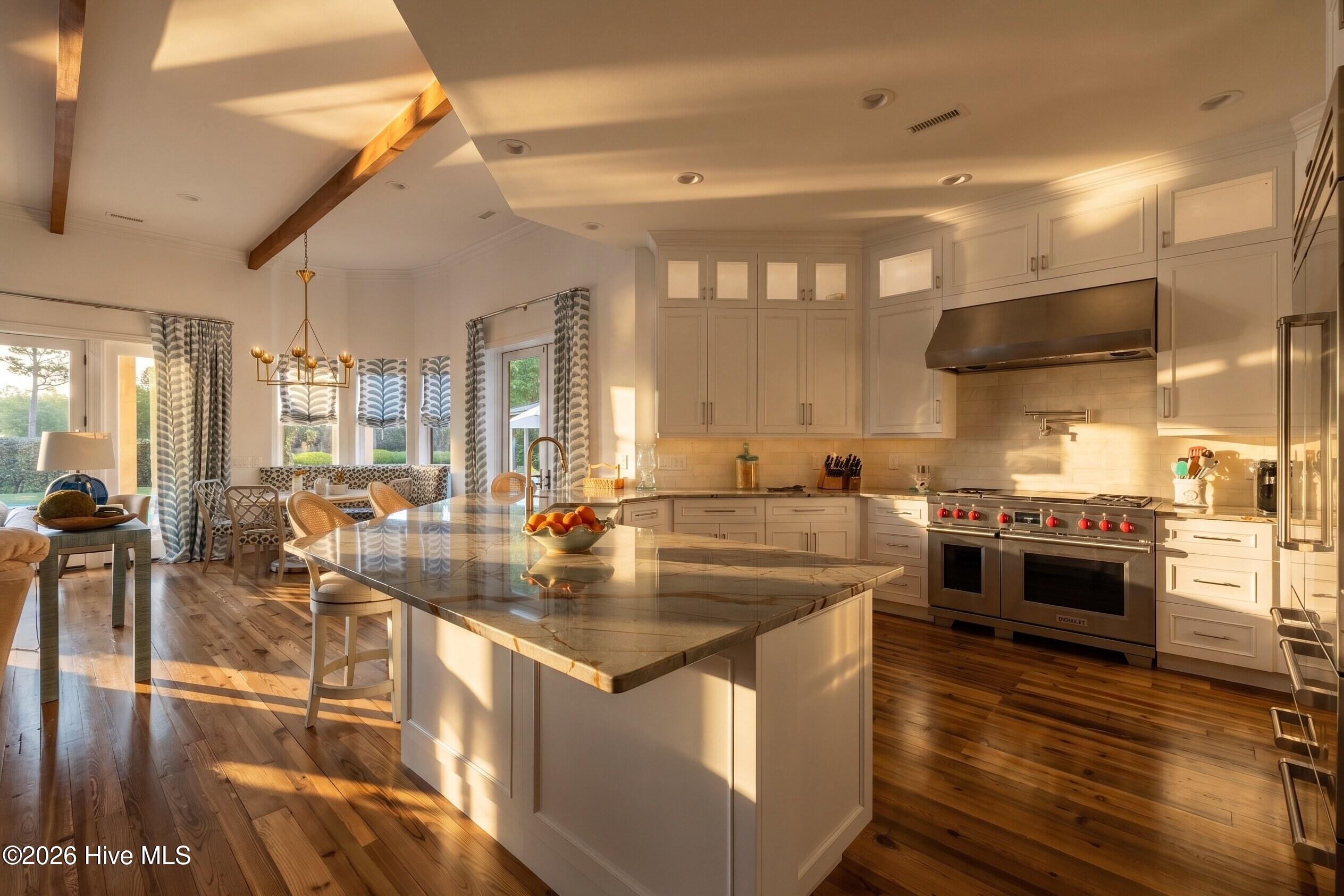 Kitchen with a large marble island, white cabinetry, stainless steel range, and adjoining breakfast nook.