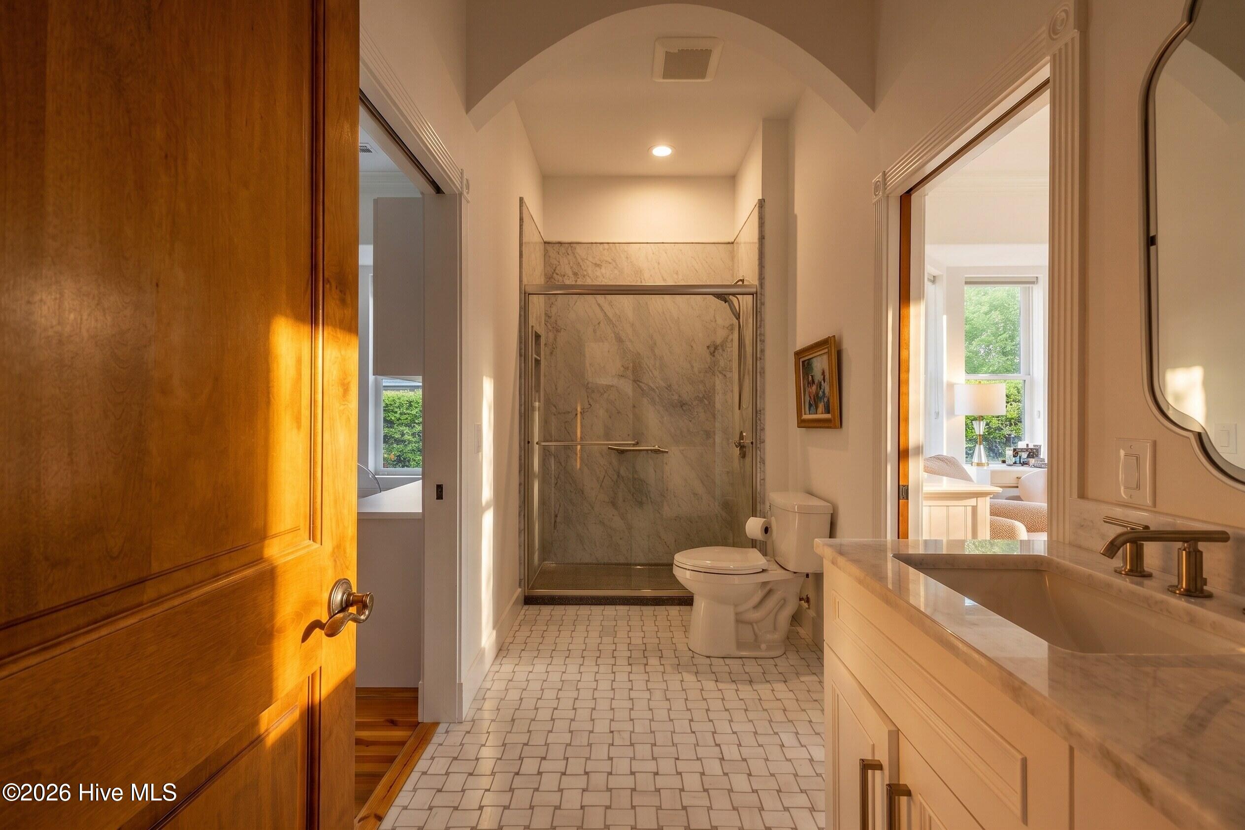 Bathroom with a marble-tiled glass shower, geometric floor tile, and sunlit wooden door.