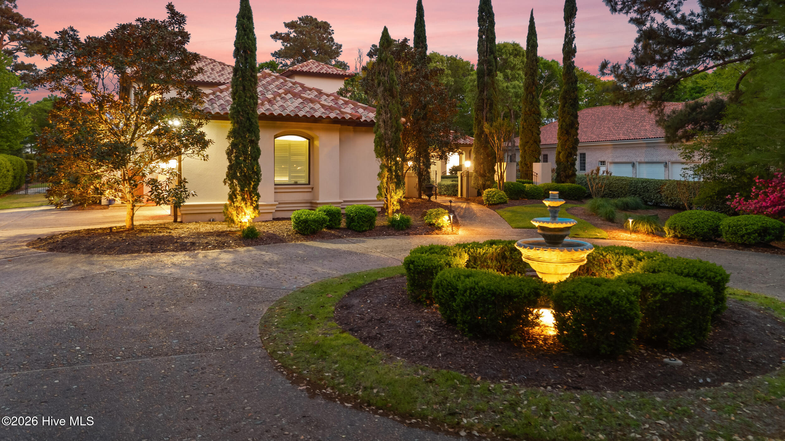Stucco home with a tile roof and landscaped courtyard fountain glowing at dusk.