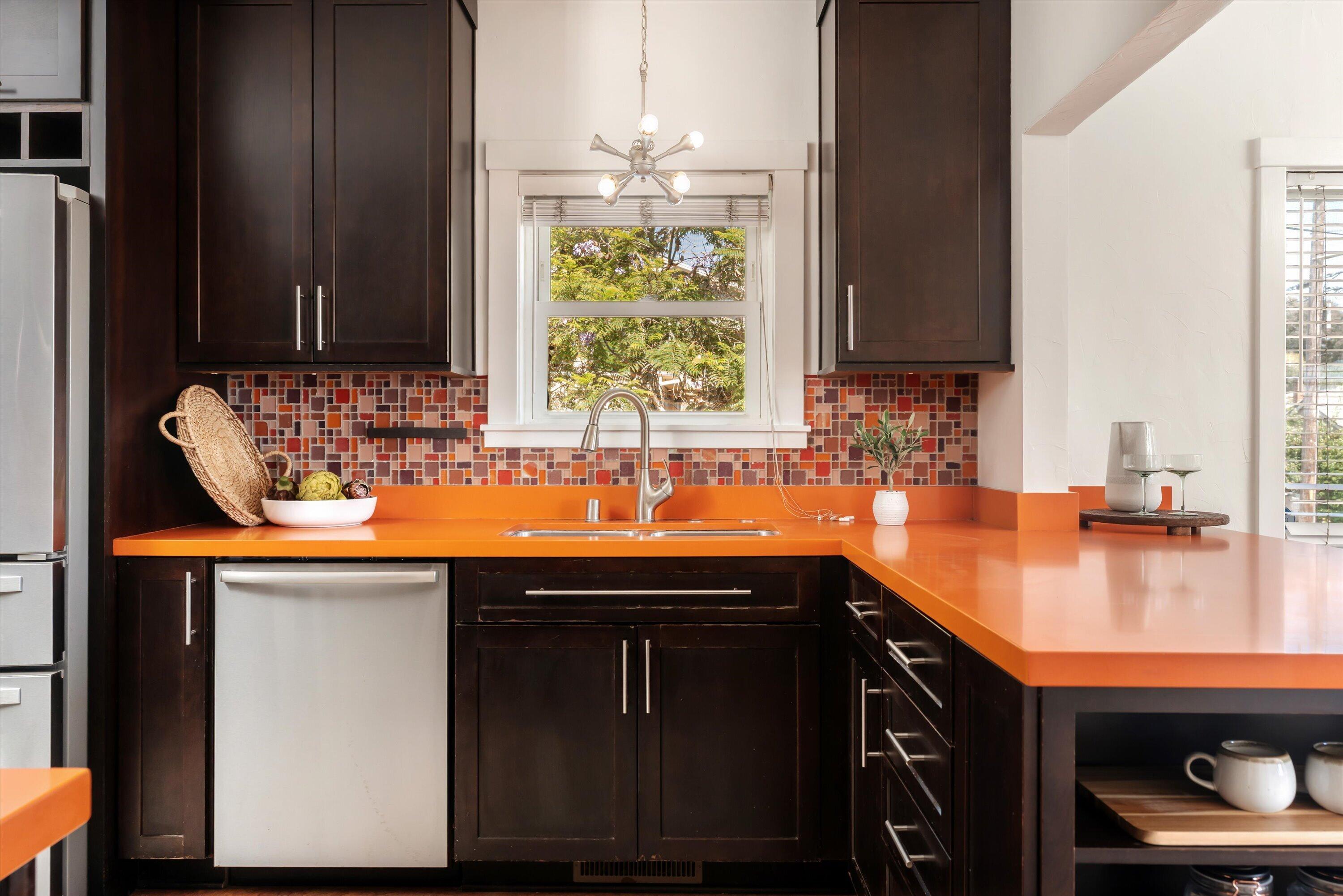 Kitchen with orange countertops, dark cabinets, and a mosaic backsplash around the window.