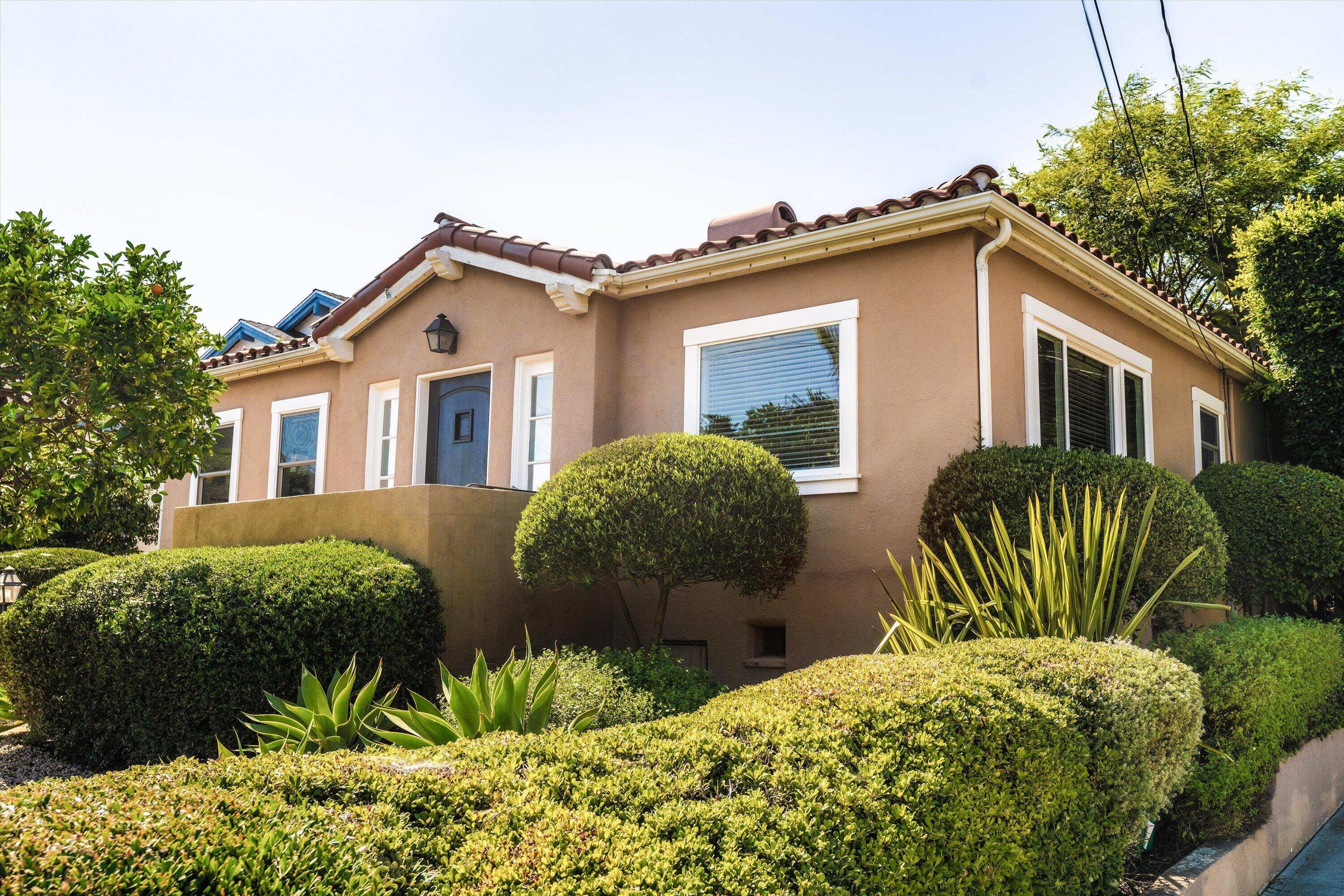 Tan stucco house with a red tile roof and blue front door, framed by neatly trimmed hedges.