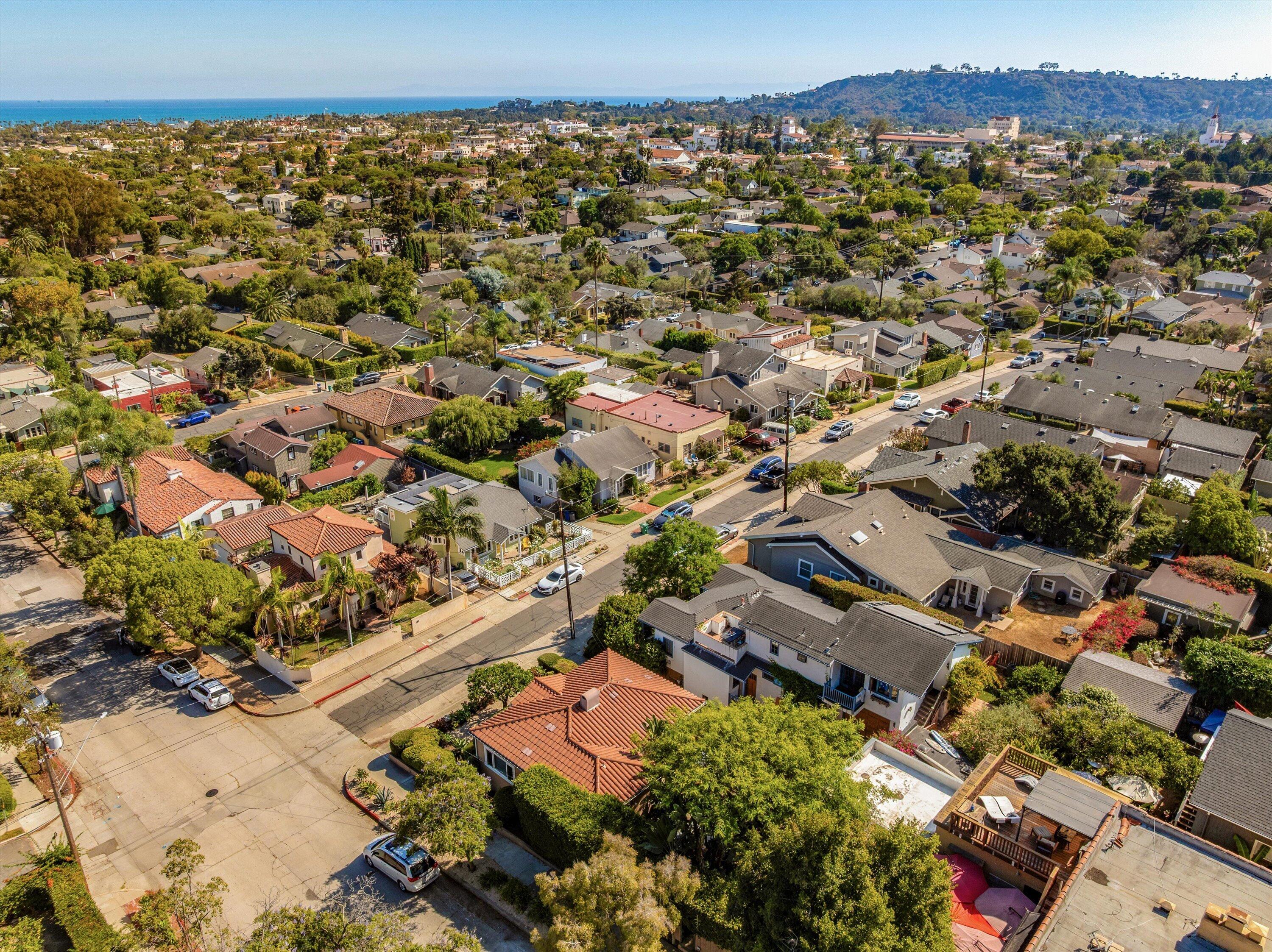 Aerial view of a residential neighborhood with the ocean and a wooded hillside in the distance.