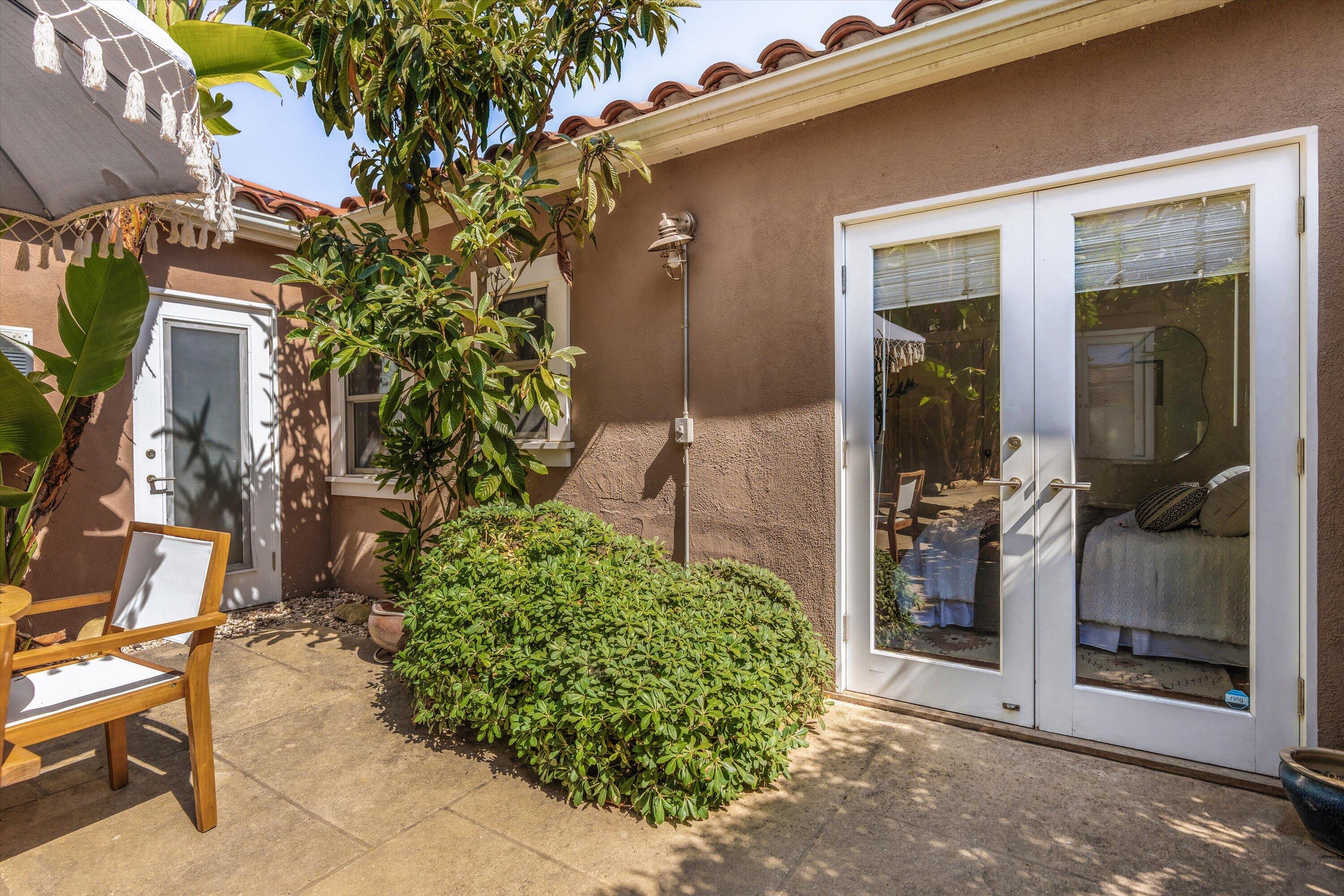 Private patio with white-framed glass doors, leafy plants, and a wooden lounge chair.