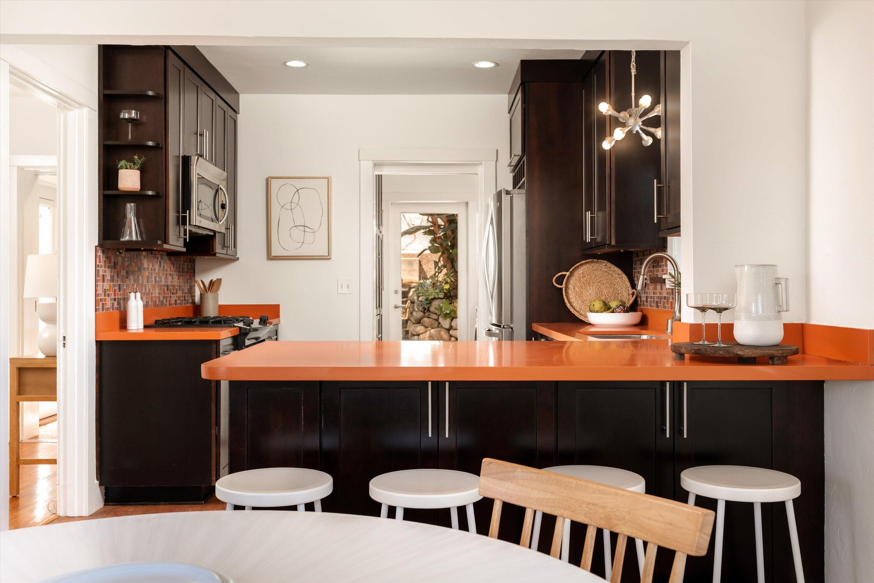 Kitchen with dark cabinets, vivid orange counters, island seating, and a garden doorway.