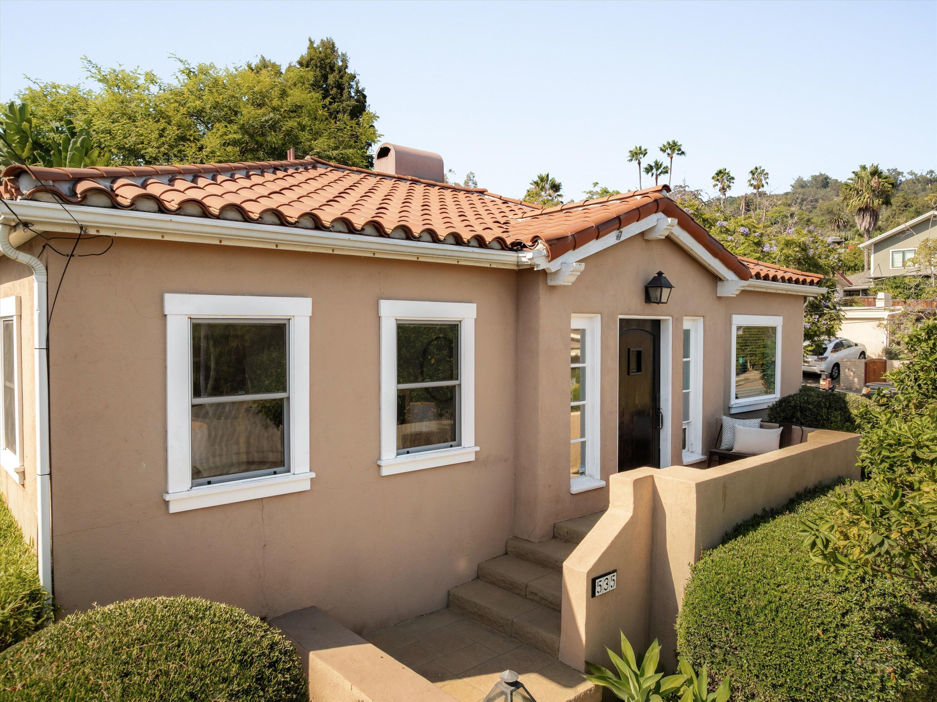 Stucco home with terracotta roof, white-trimmed windows, and a hedge-lined entry courtyard.