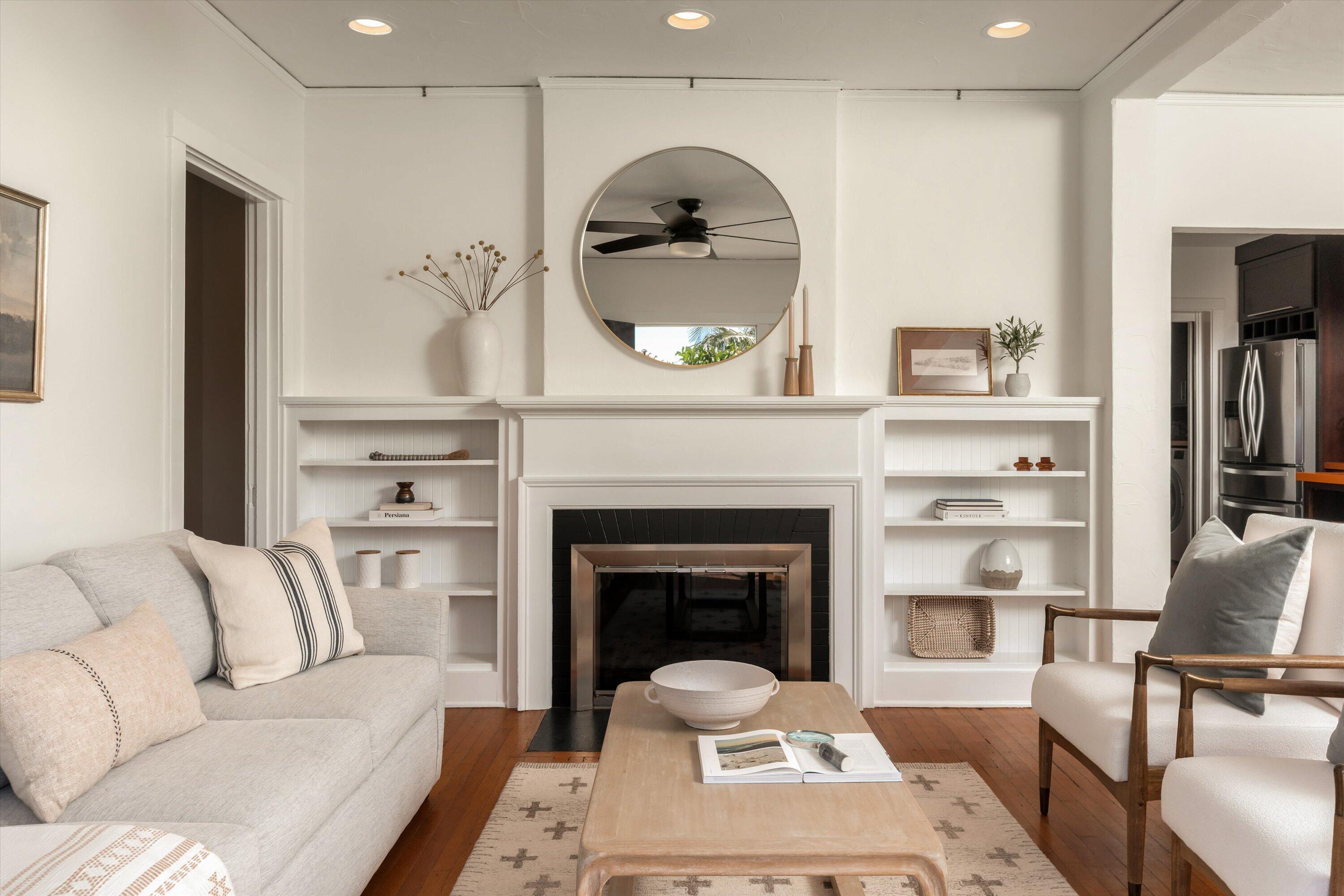 Living room with a white fireplace, built-in shelves, light sofa, and wood-framed chairs.