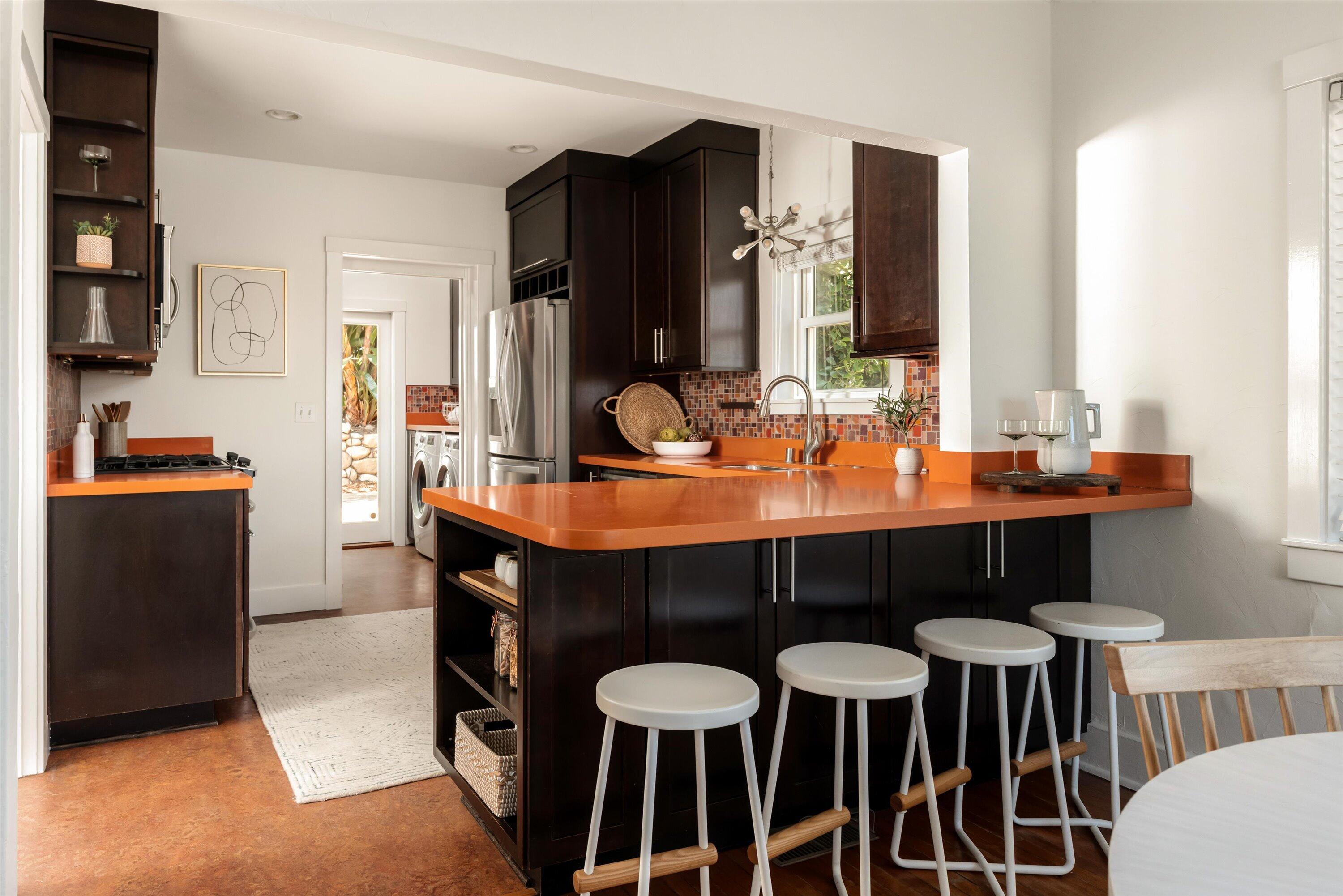 Kitchen with dark cabinetry, a burnt-orange island countertop, mosaic backsplash, and white stools.