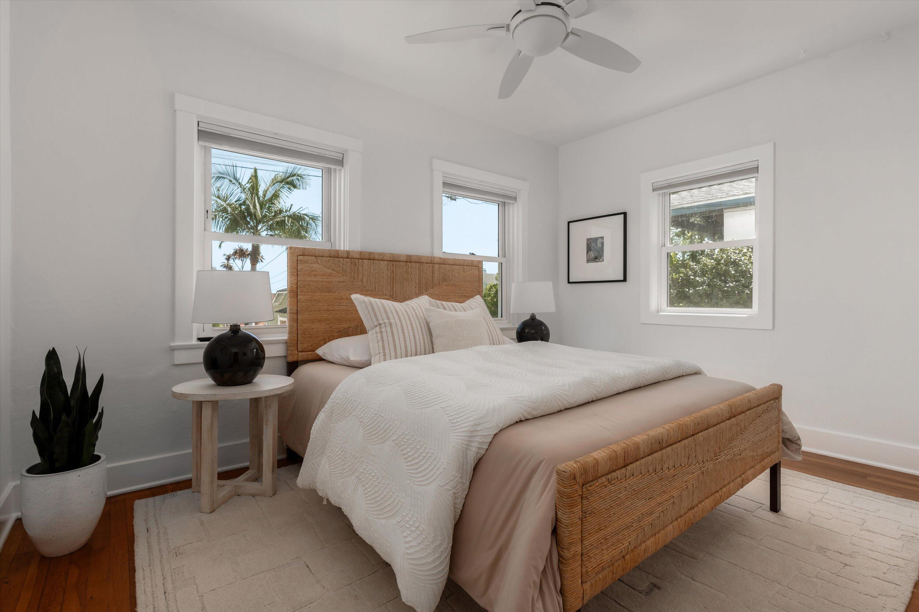 Bedroom with a woven rattan bed, white textured bedding, and windows overlooking palm trees.