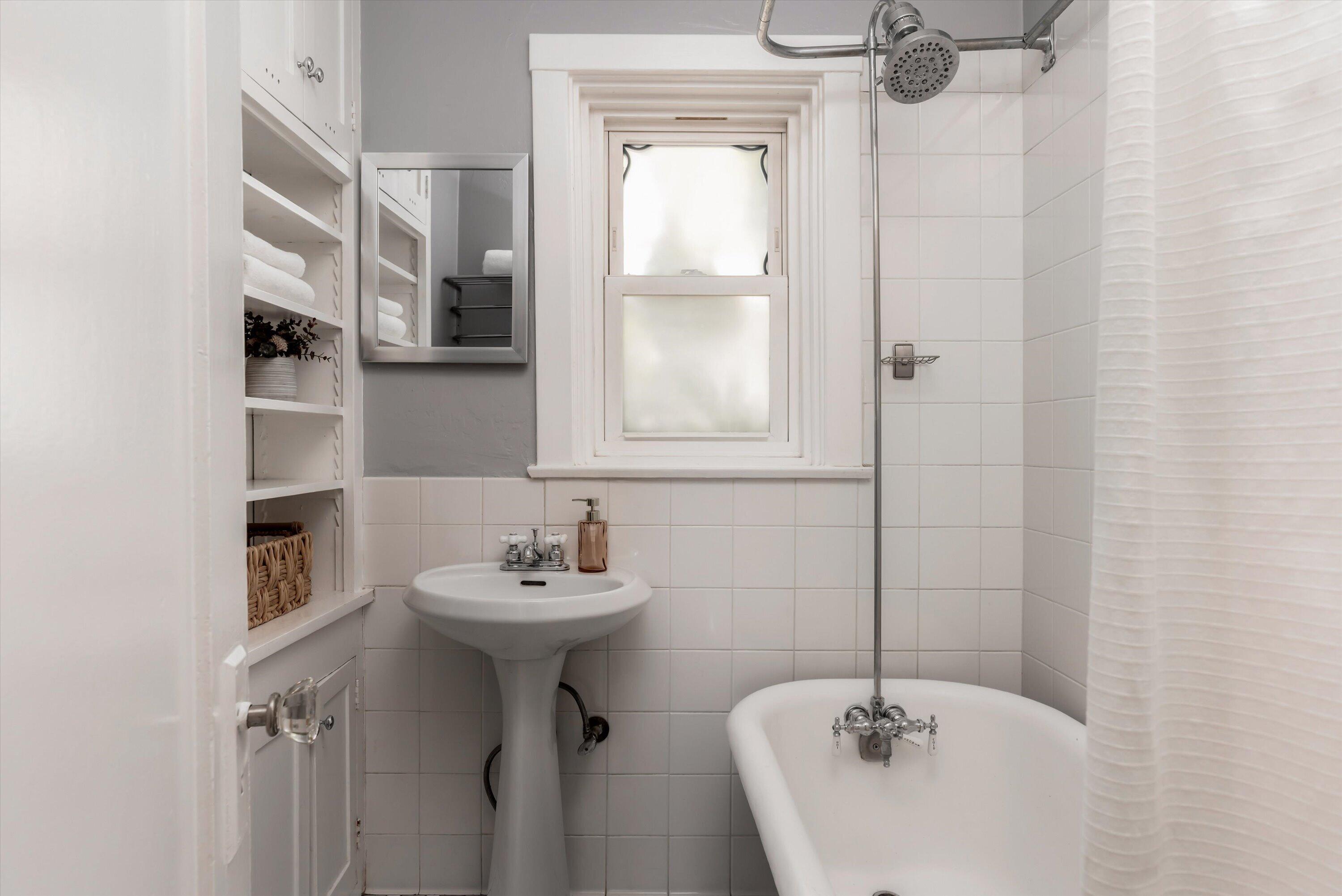 Bathroom with a pedestal sink, freestanding tub, overhead shower, and built-in towel shelves.