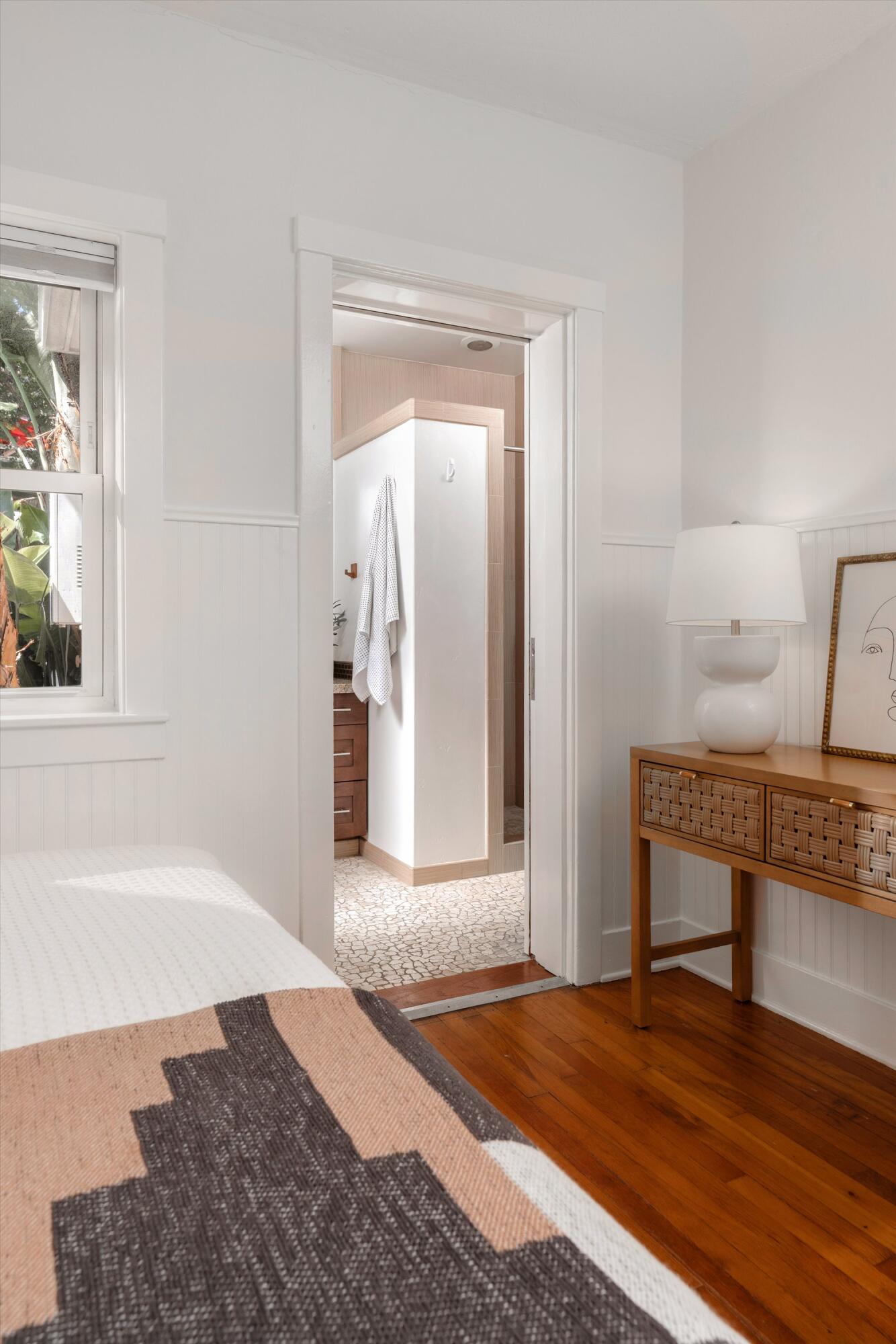 Bedroom with hardwood floors and a view through the open doorway into a tiled bathroom.