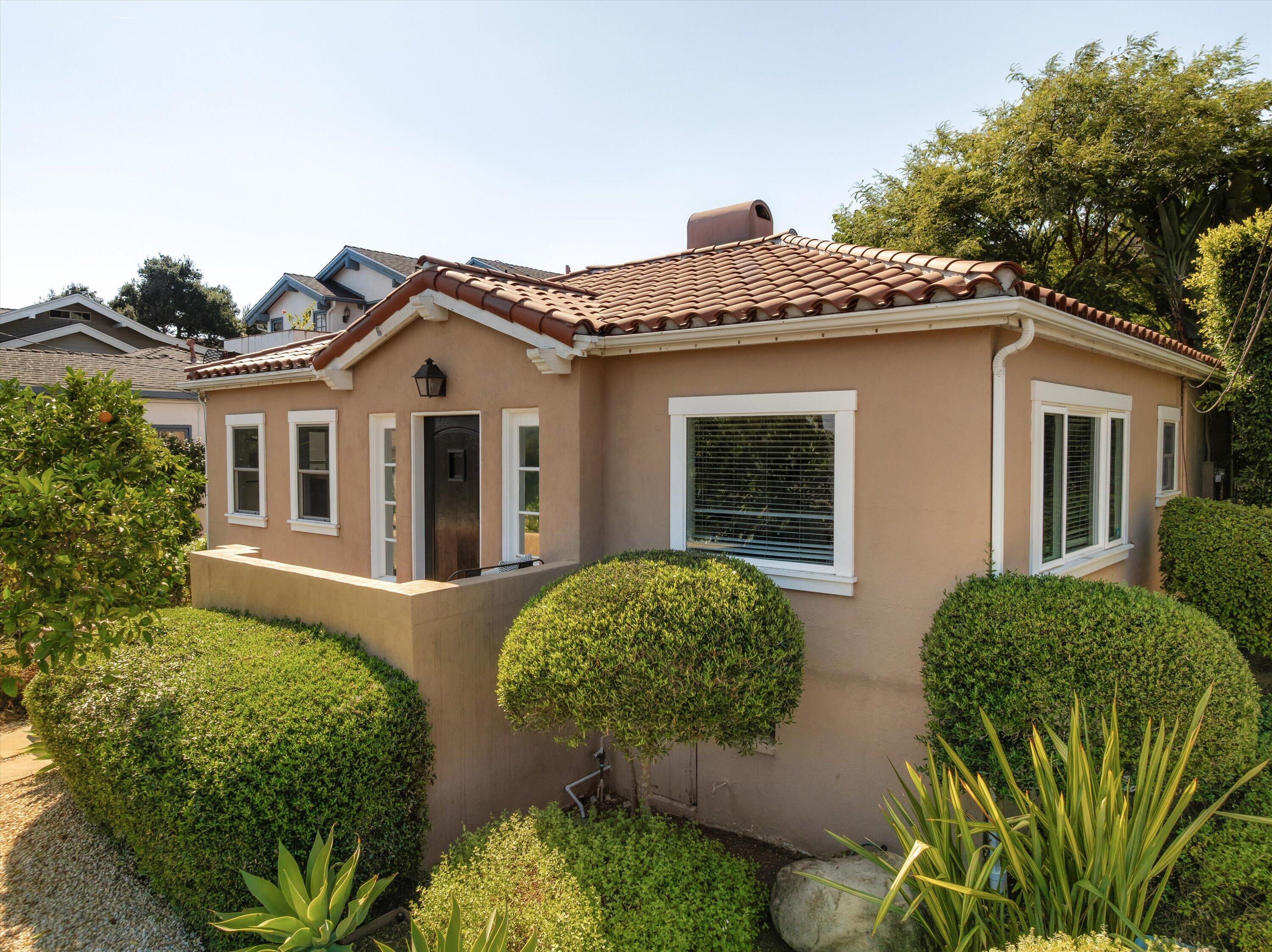 Single-story stucco house with a terracotta tile roof, dark entry door, and clipped front garden shrubs.