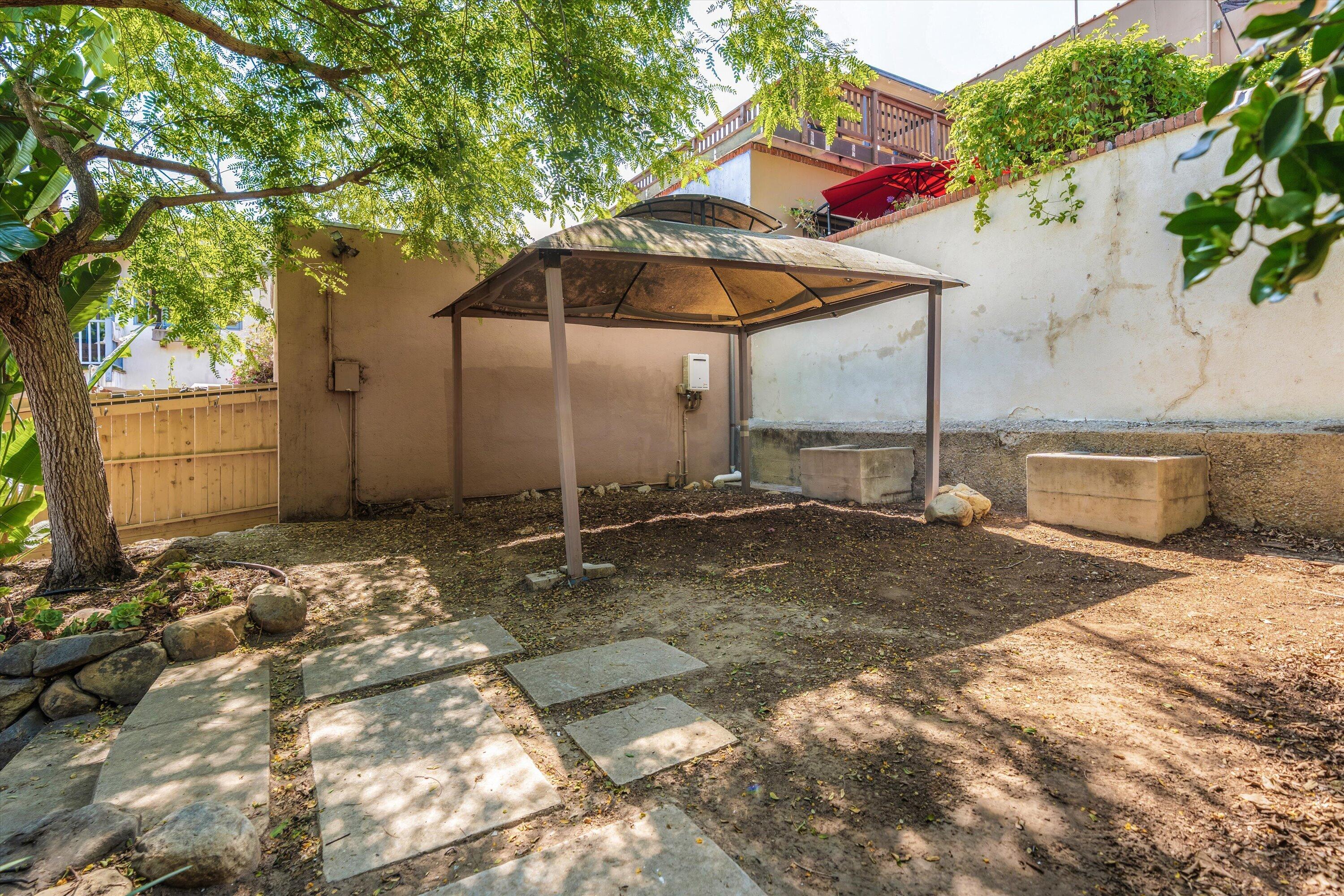 Backyard with a metal gazebo, stone stepping path, mature shade tree, and wooden gate.