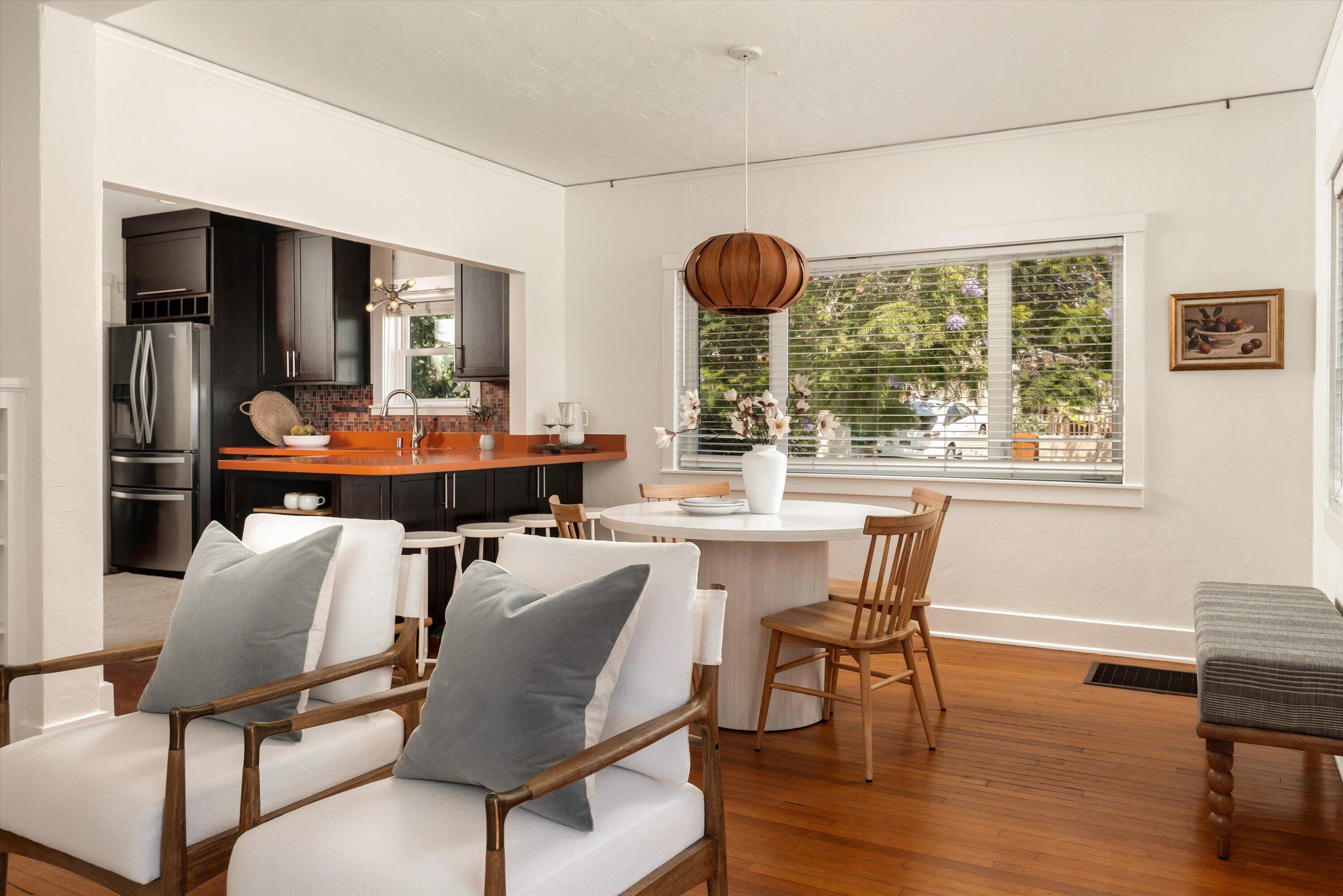 Open-plan dining and living area with dark kitchen cabinets, orange countertops, and hardwood floors.