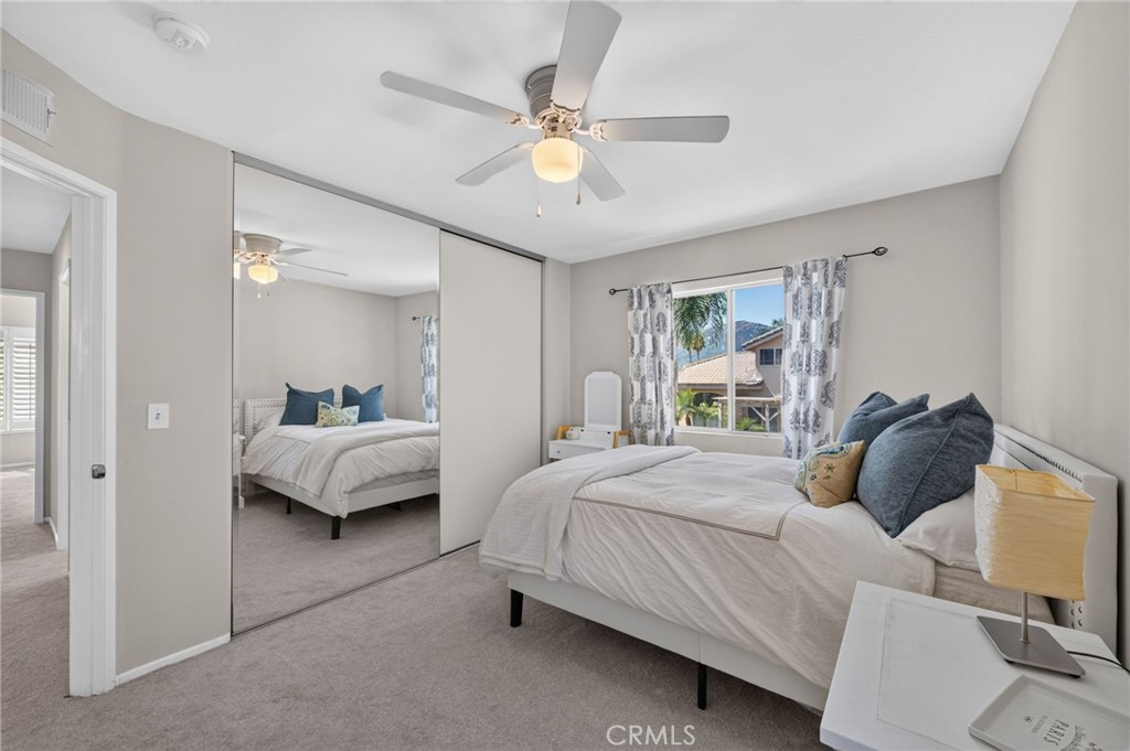 Bedroom with mirrored closet doors, blue accent pillows, and a ceiling fan.