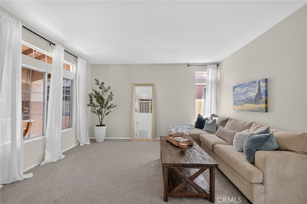 Staged living room with a tan sofa, rustic coffee table, and large curtained windows.