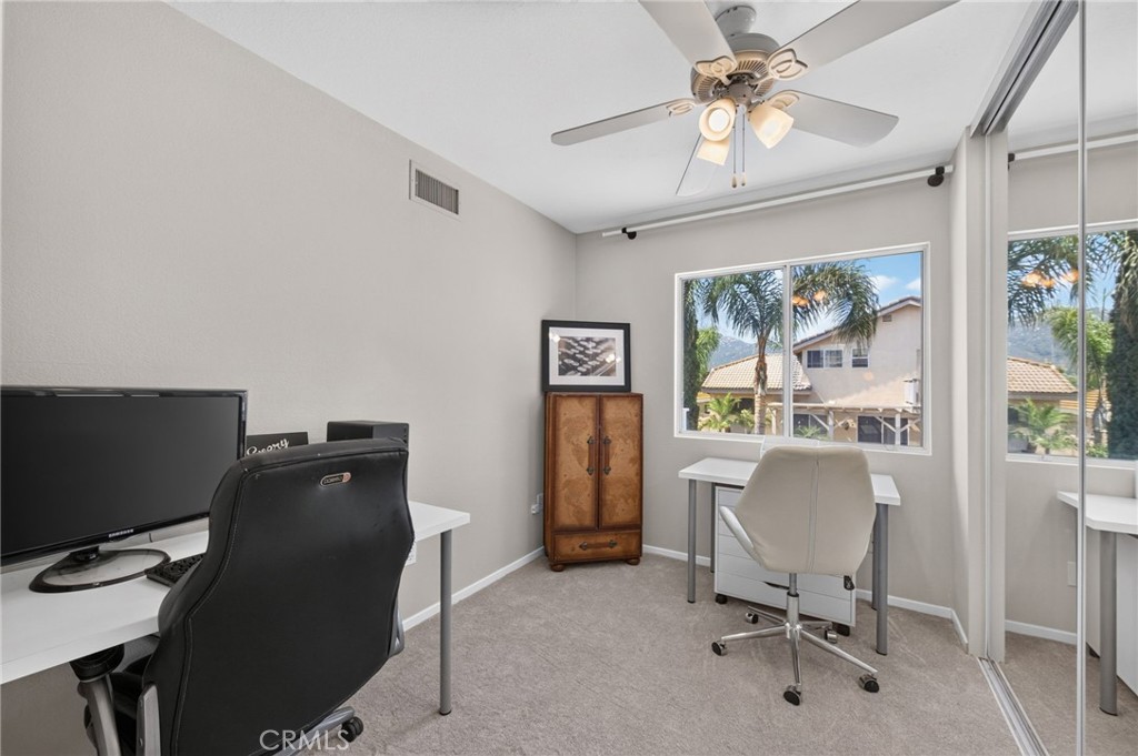 Home office with two desks, mirrored closet doors, and windows overlooking palm trees.