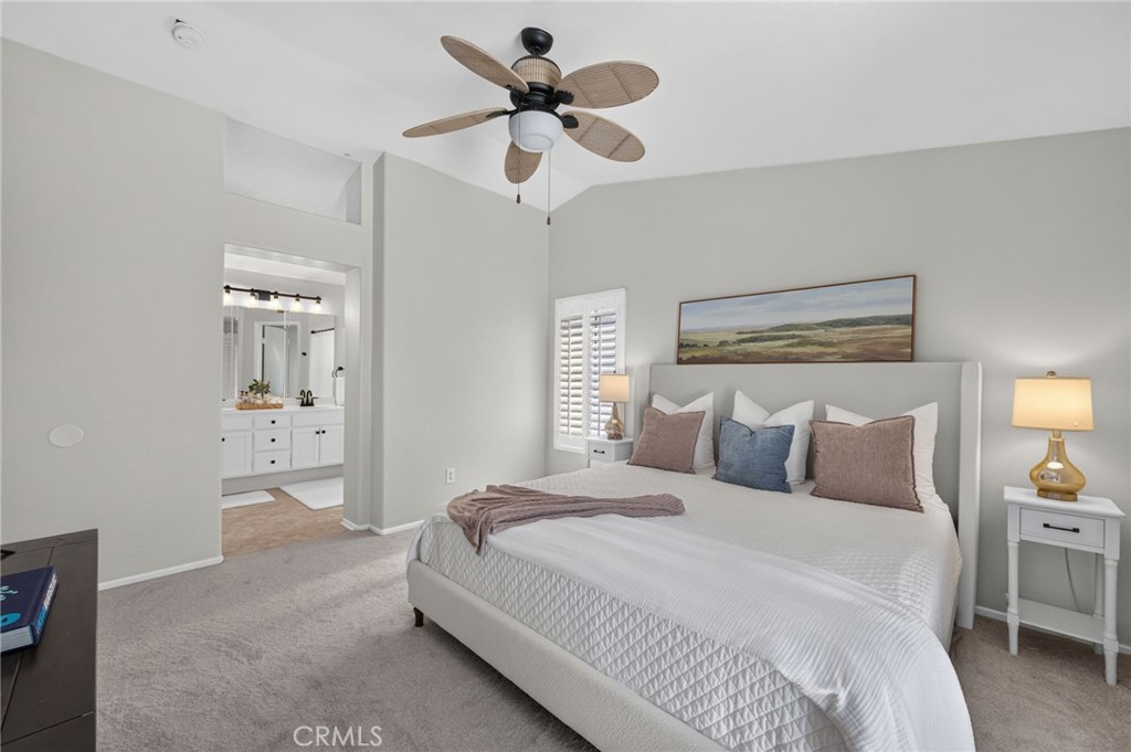 Primary bedroom with a white bed, ceiling fan, and open doorway to a bathroom.