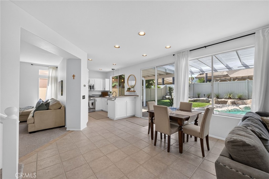 Open-plan dining room and kitchen with tiled floors and windows overlooking a backyard pool.