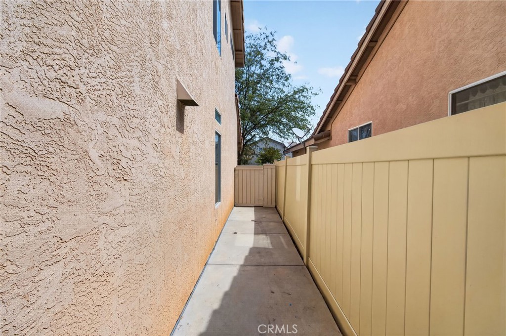 Side walkway between the stucco house and a tan privacy fence, ending at a gate.