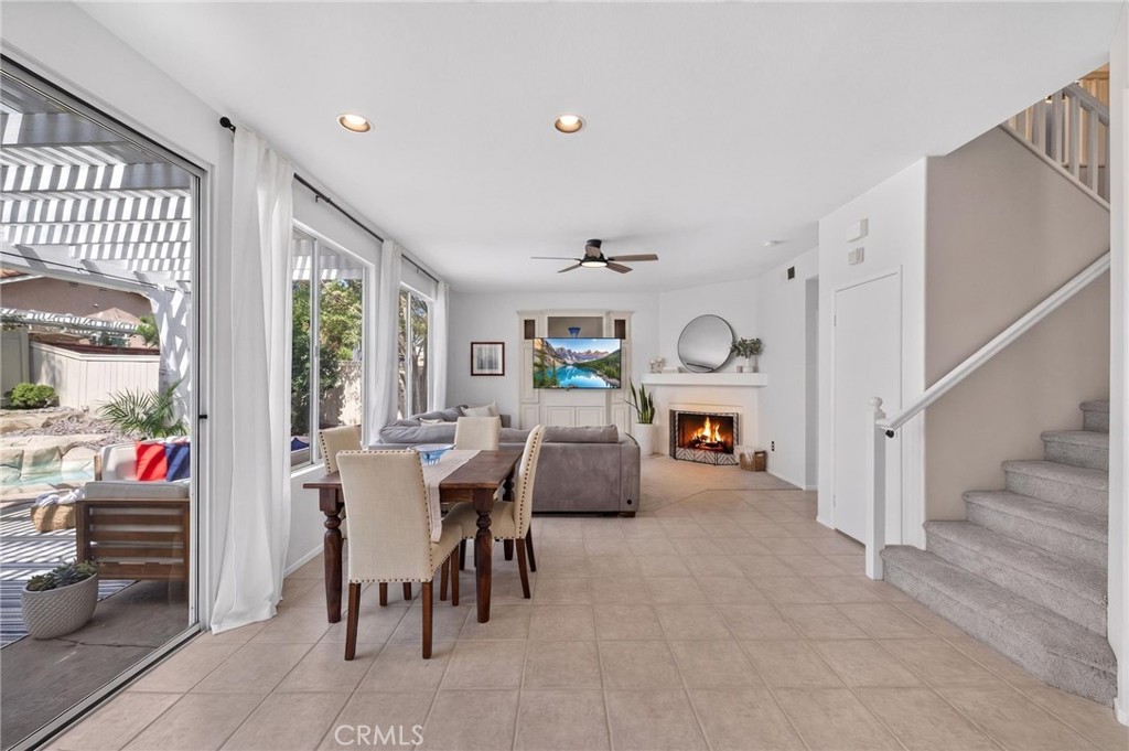 Open-plan living and dining room with a fireplace, staircase, and sliding doors to a covered patio.