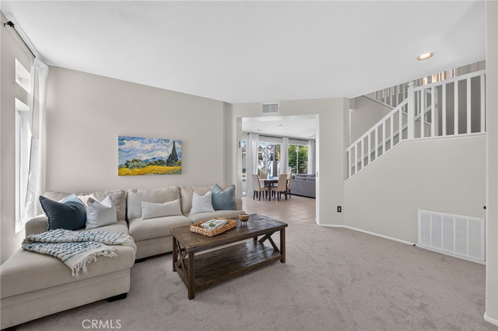 Living room with a beige sectional, dark wood coffee table, and staircase beside an open dining area.