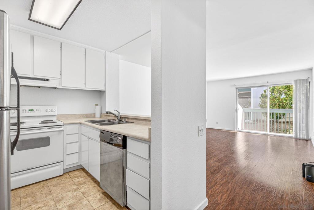 Apartment kitchen opening to an empty living area with sliding glass doors to a balcony.
