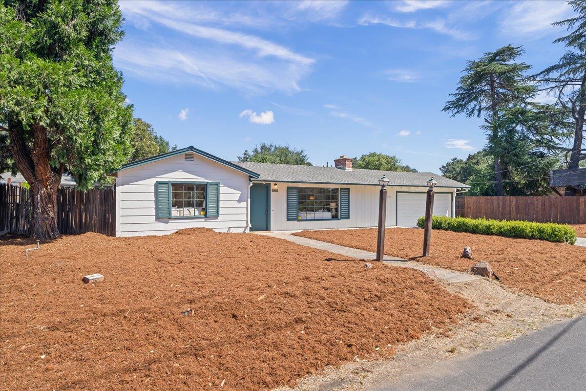 Single-story house with teal shutters, attached two-car garage, and a broad mulched front yard.