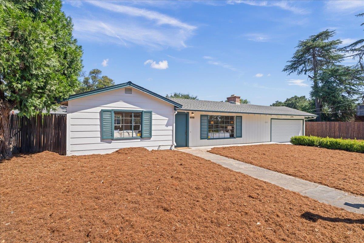 Single-story white home with teal trim, a garage, and a freshly mulched front yard.